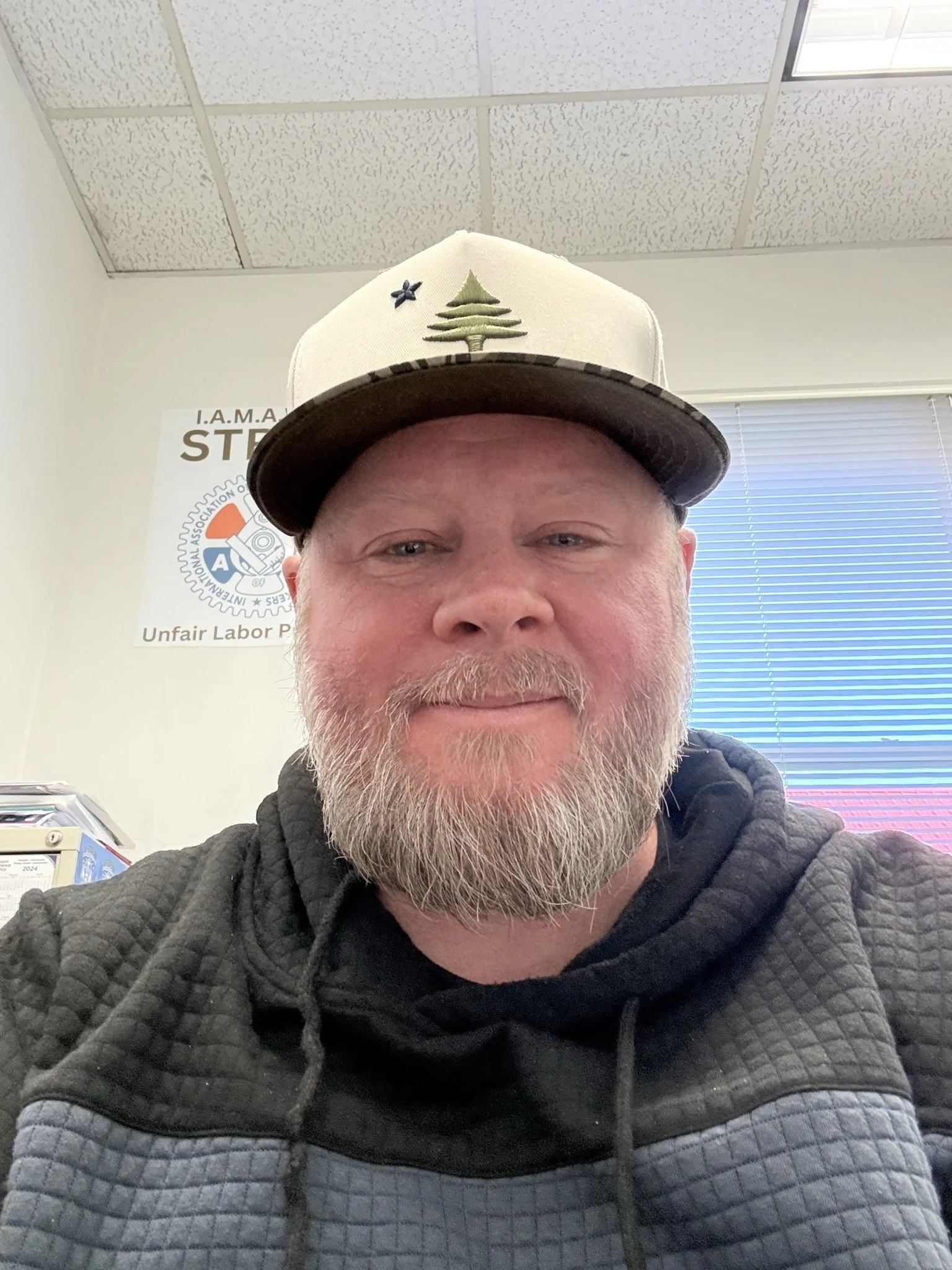 Close-up portrait of a young man with dark hair and green eyes, wearing a white shirt, against a plain background.