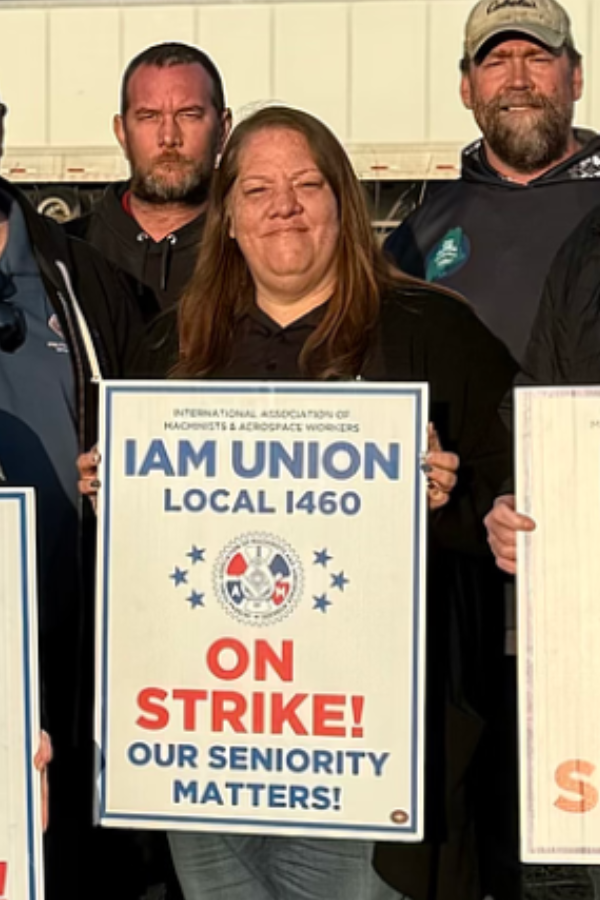 A smiling woman with long brown hair, wearing a white shirt, maroon cardigan, and black leather skirt, standing against a plain white background.