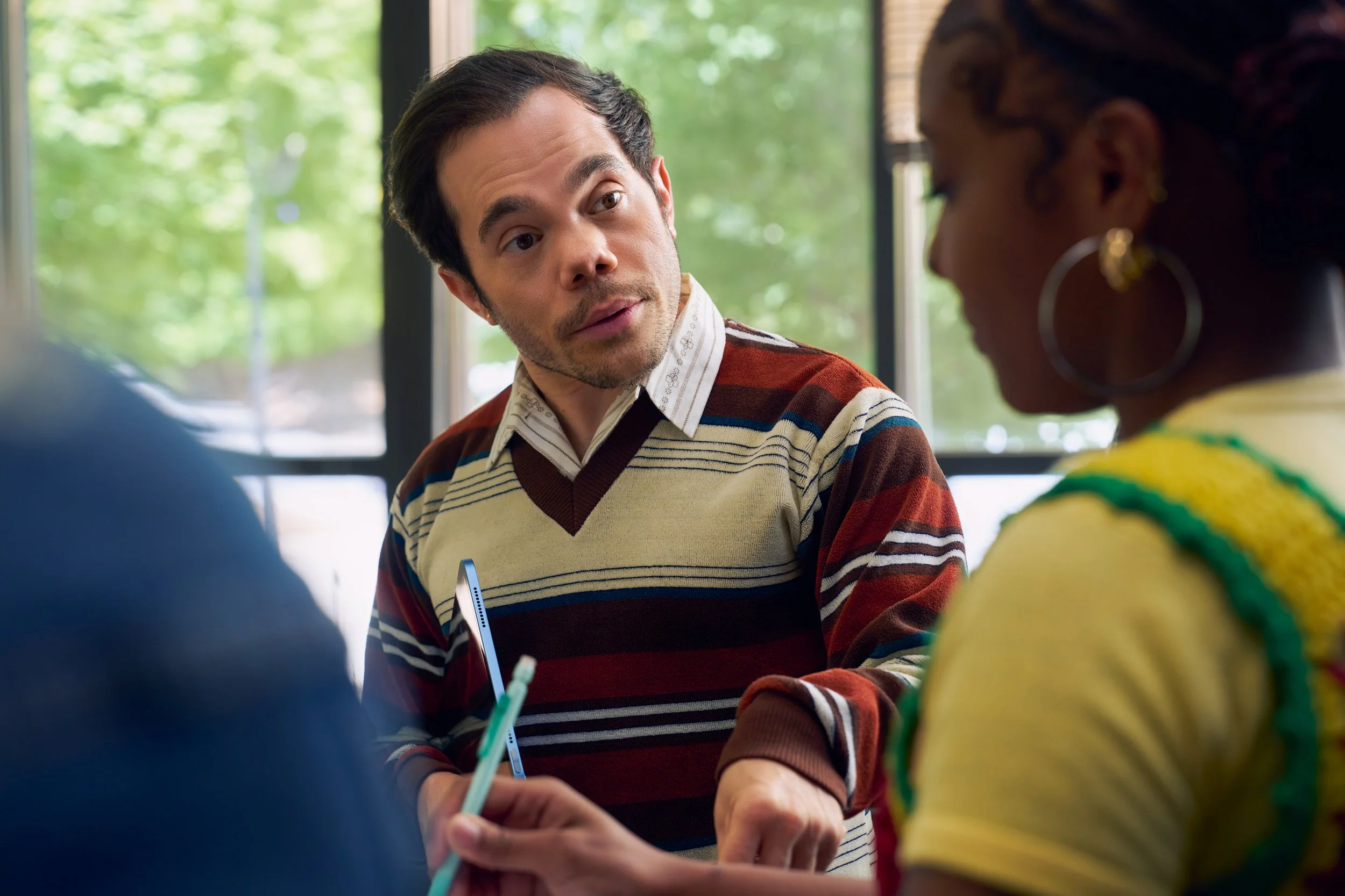 A white professor who has dwarfism stands next to a student in his class as he speaks to her.