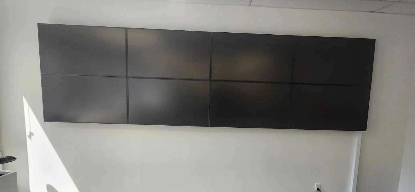 Wall-mounted black TV screen with six panels on a white wall in a room.