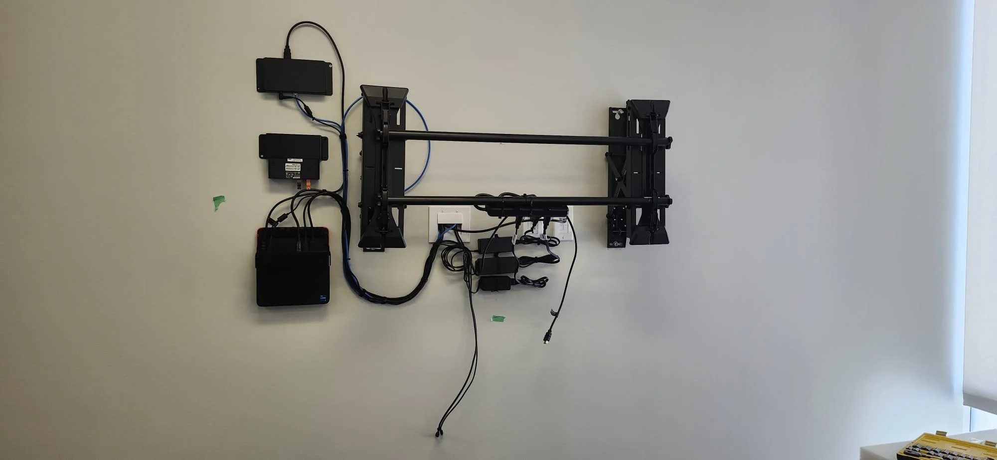 Wall-mounted mechanical setup with various black electronic components, wires, and metal frames.