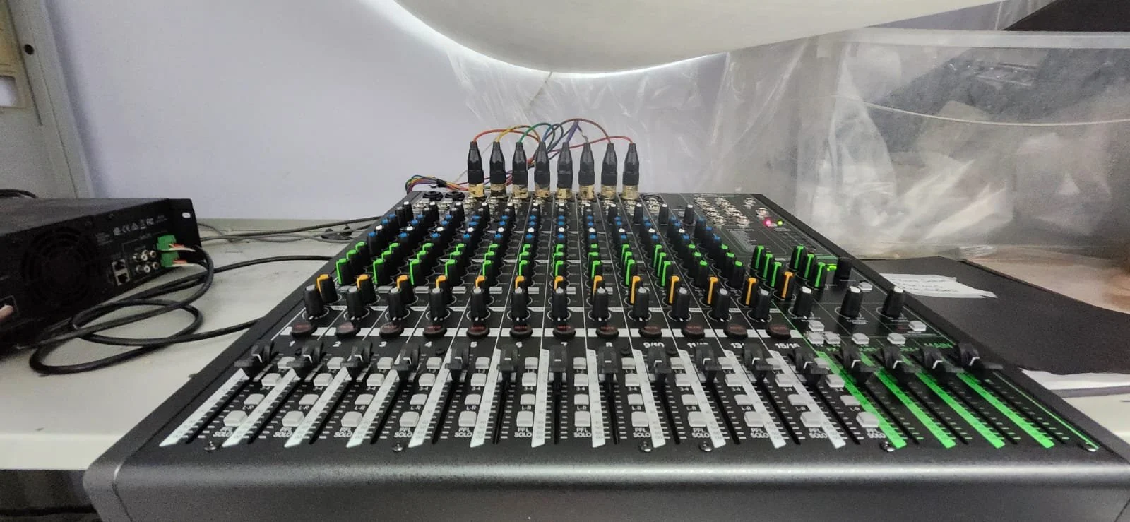Audio mixing console with numerous sliders, knobs, and cables, situated on a table in a technical or event setup.