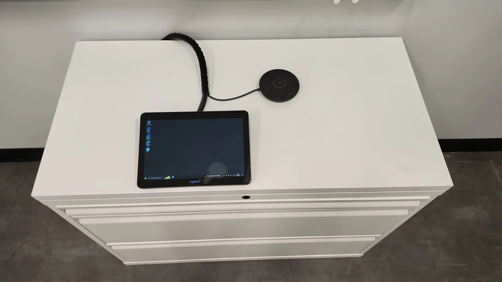 White filing cabinet with a tablet and a circular conference speakerphone on top, connected by a cable.