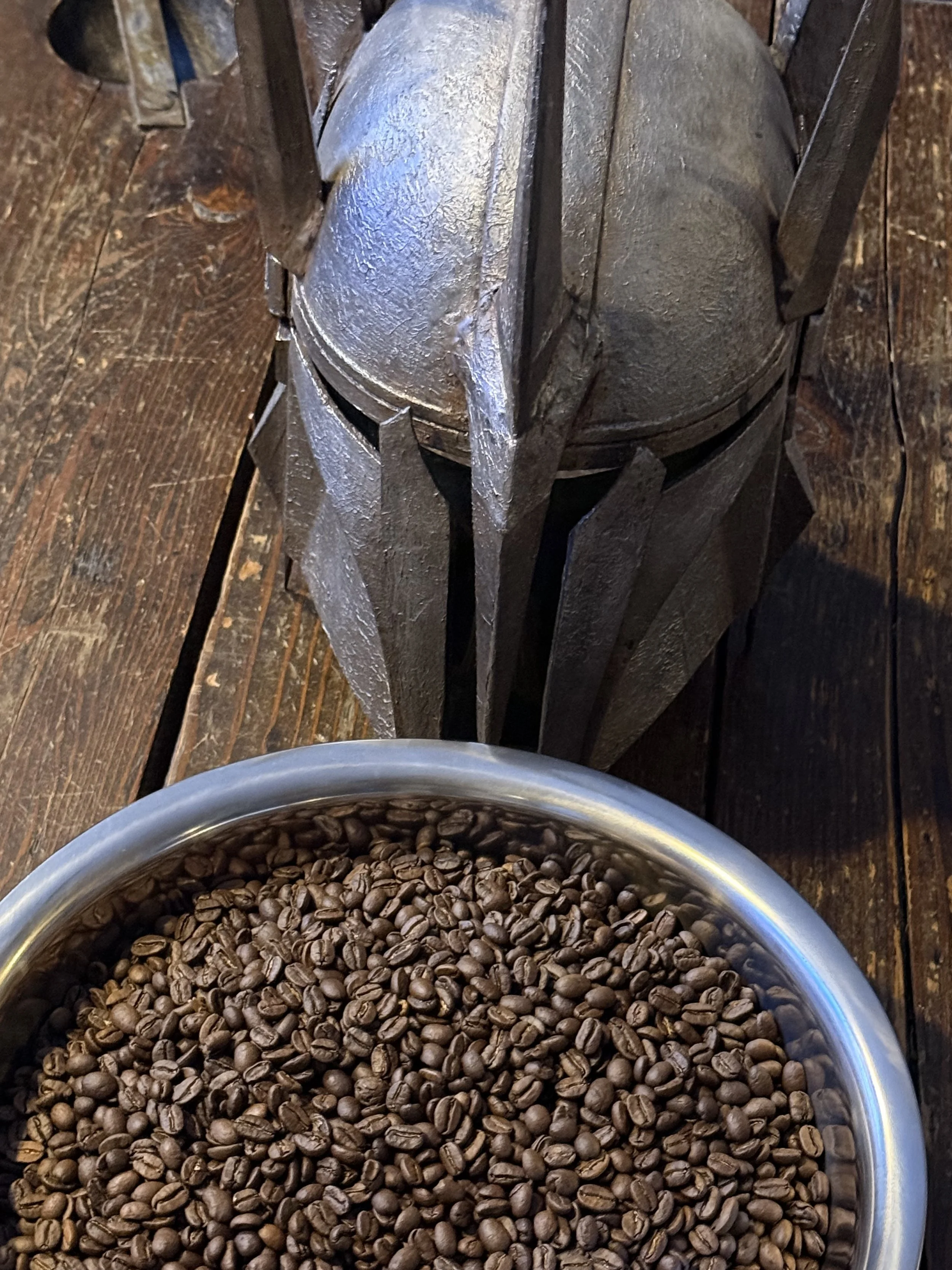 A metal coffee grinder with a wooden handle and a bowl of roasted coffee beans on a wooden surface.