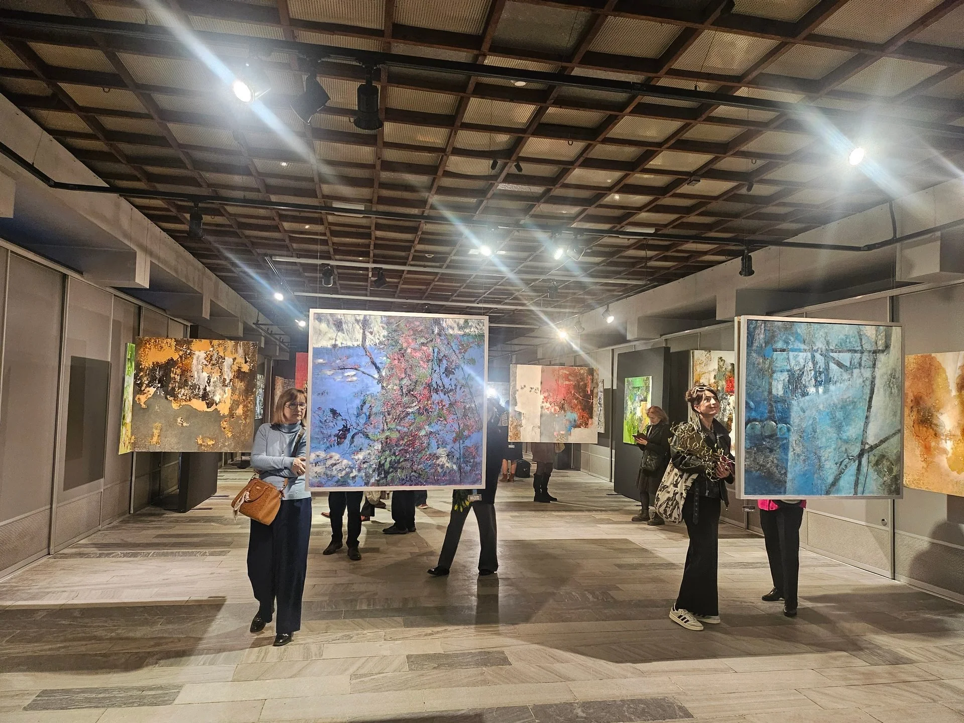 Visitors observing paintings during a diverse contemporary art exhibition featuring multiple styles