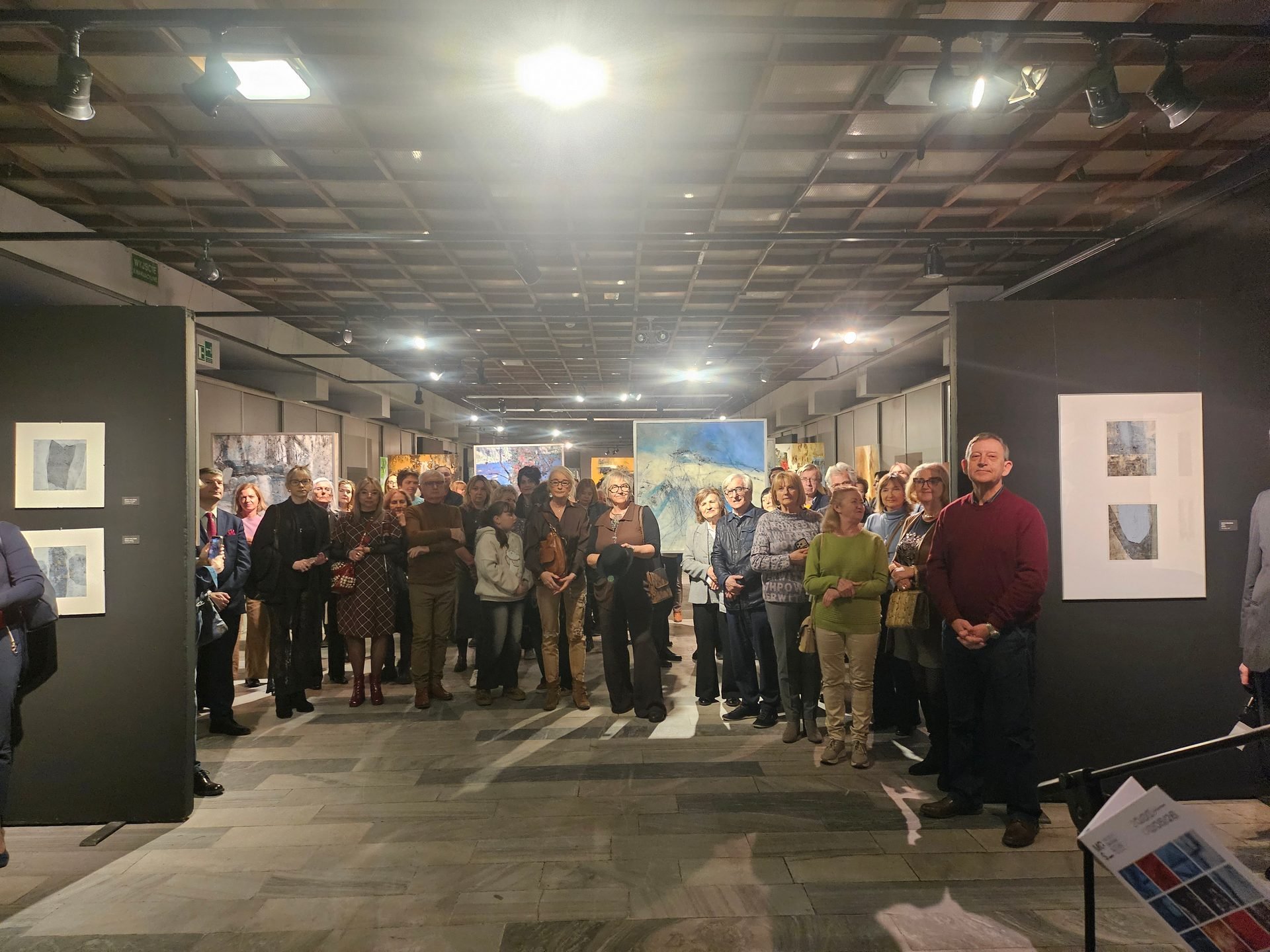 Group of visitors at an art gallery exhibition, standing in the exhibition space and looking directly at the camera