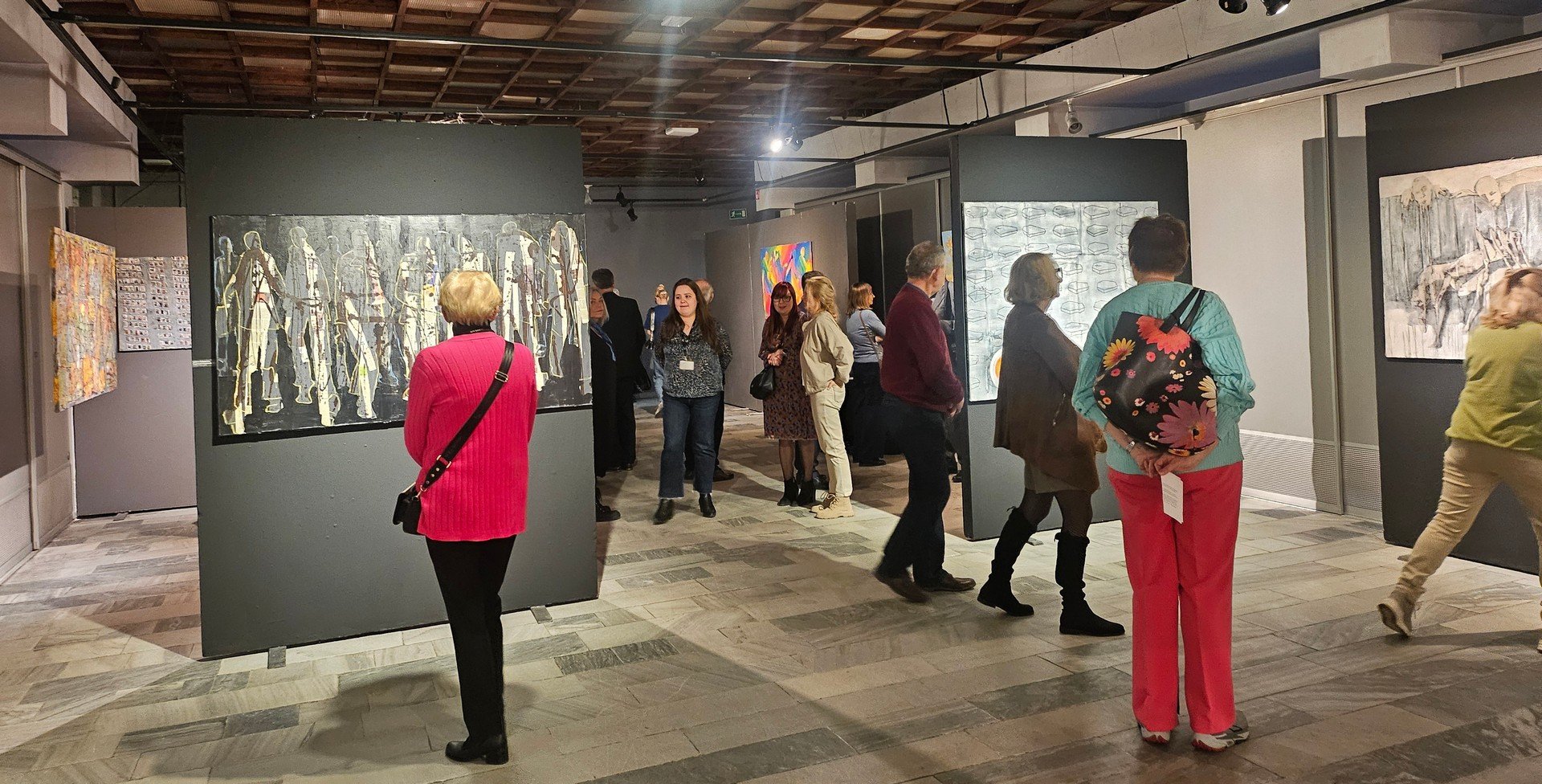 Visitors observing paintings by Monika Ślósarczyk during a contemporary art exhibition in art gallery space