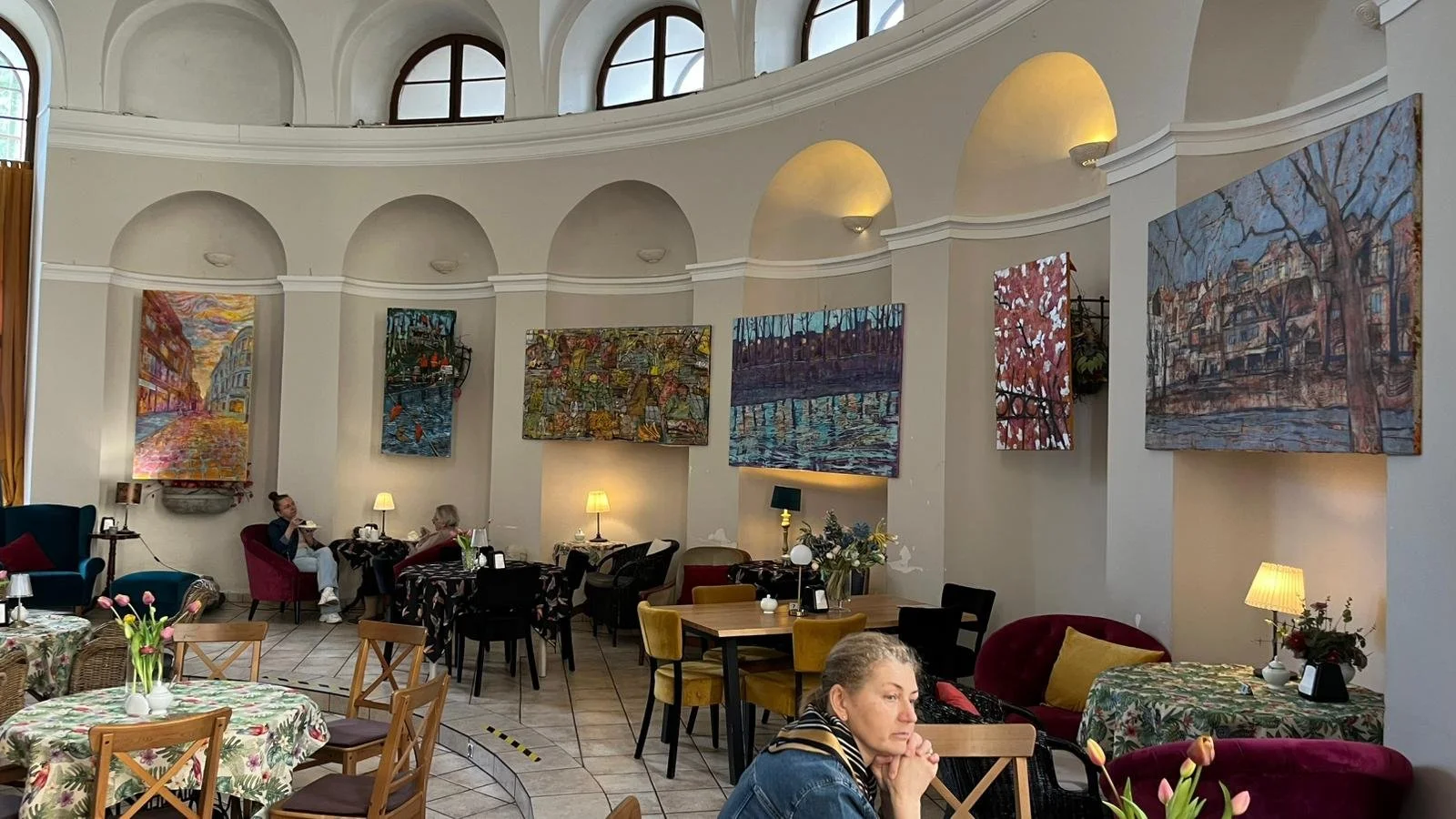 Exhibition view showing six contemporary landscape paintings displayed on a cafe walls.