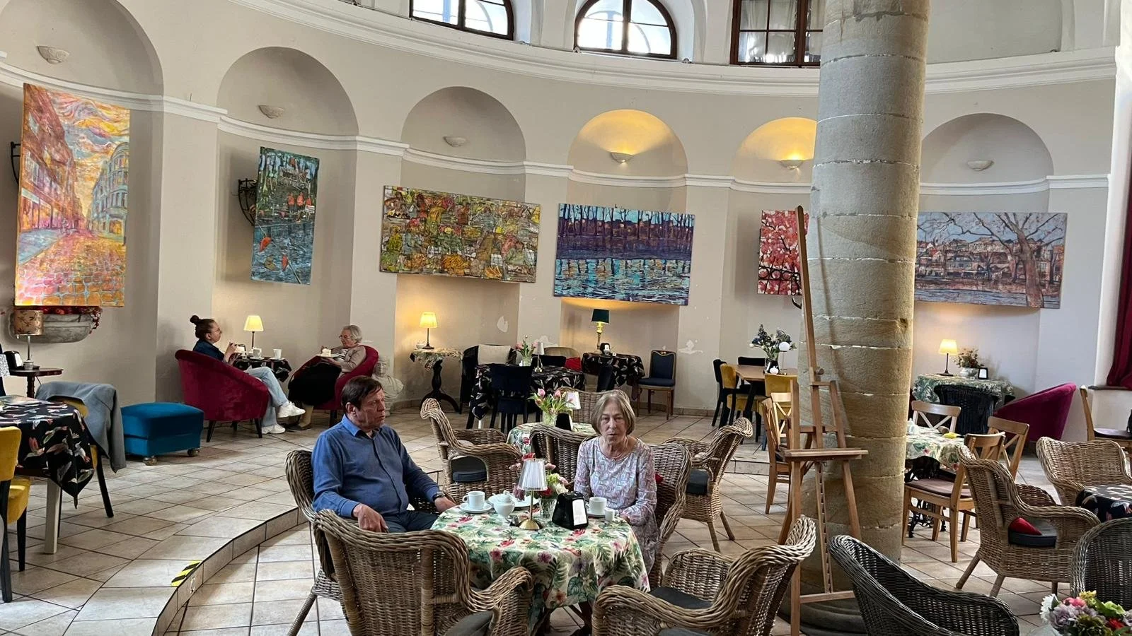 Exhibition view of Monika Ślósarczyk "Weduta i pejzaż miejski ze sztafażem" paintings displayed on walls in a cafe interior