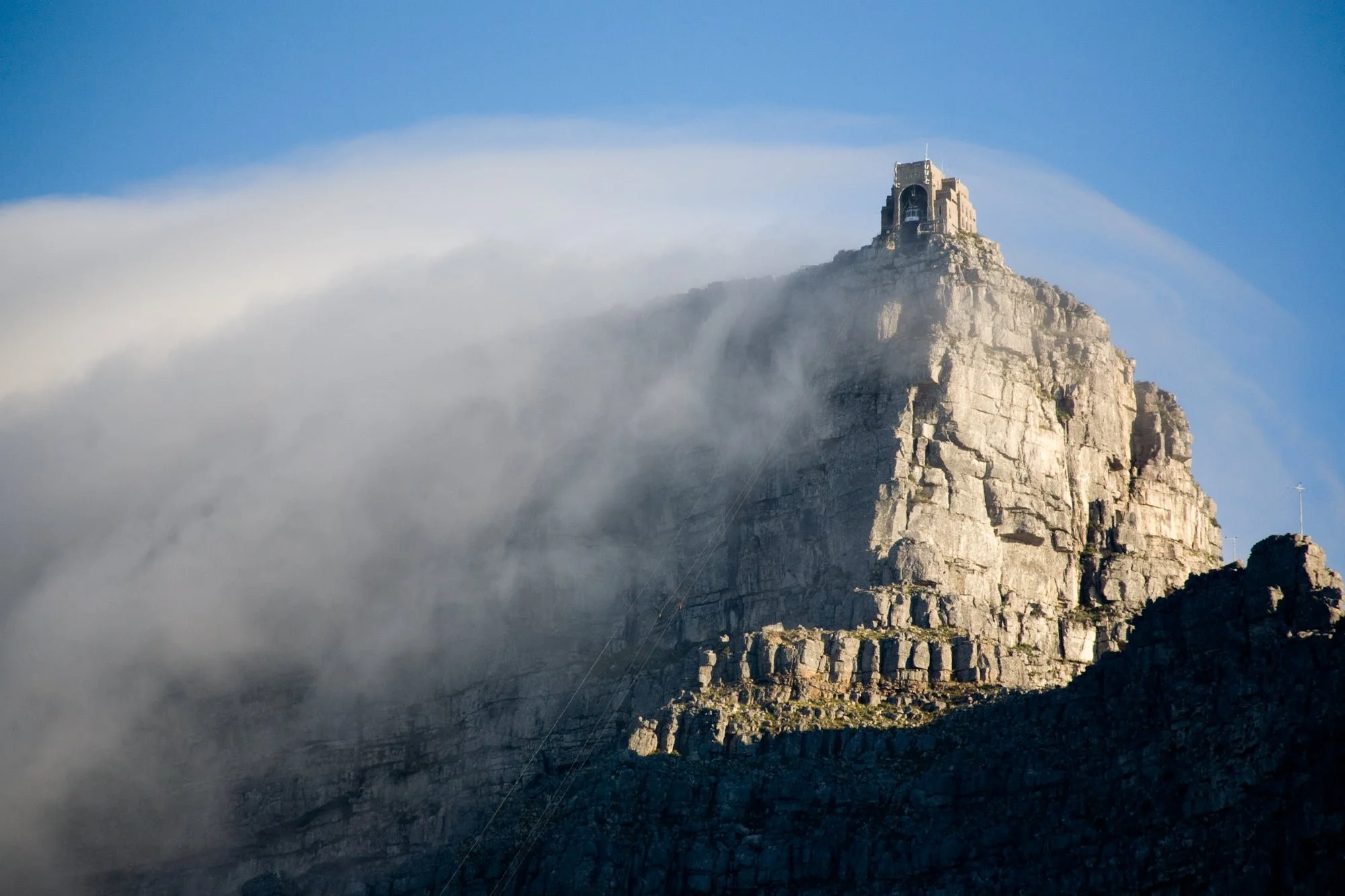 A mountain with a structure on top and clouds surrounding it.