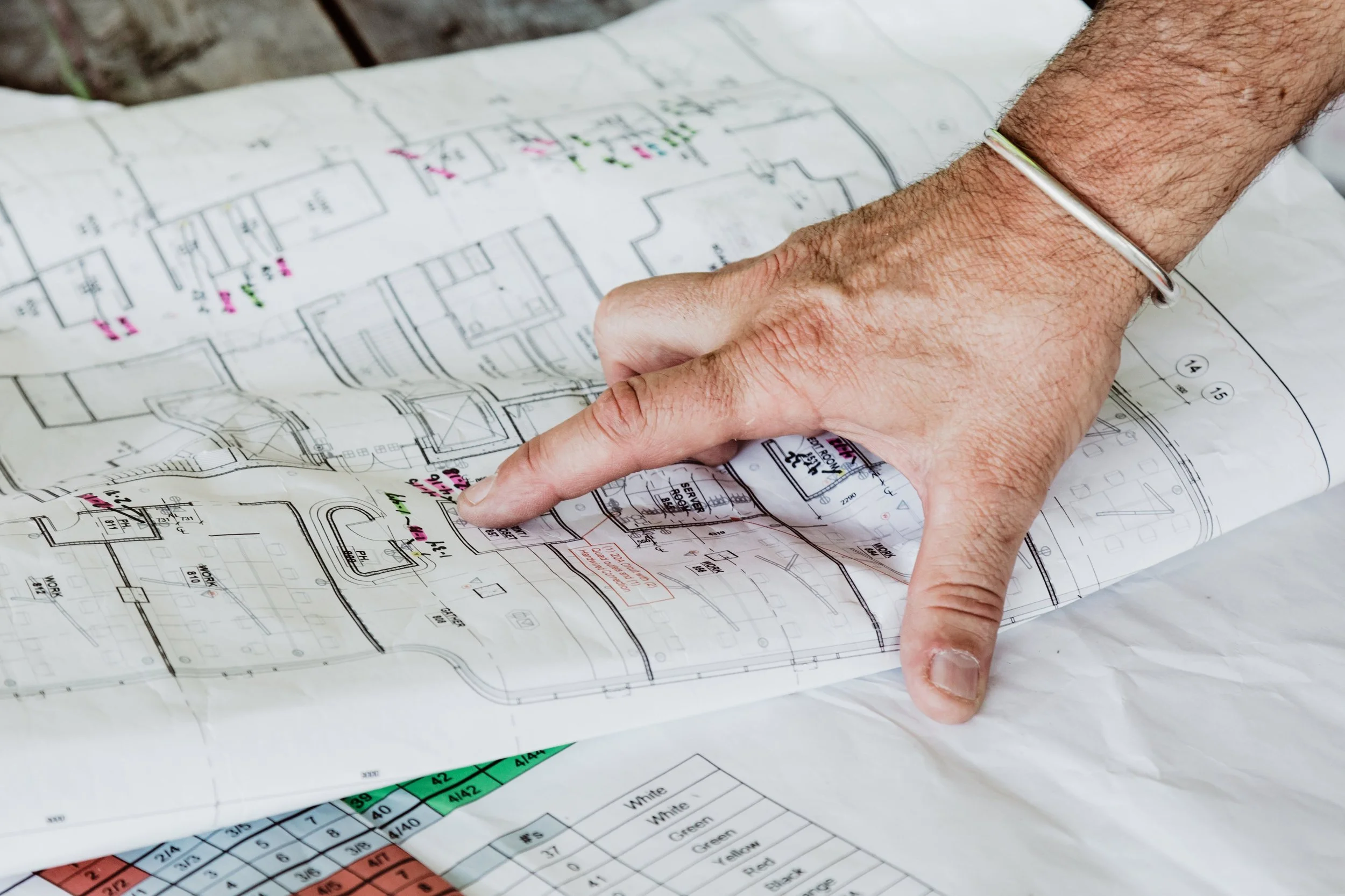 A person pointing at an architectural blueprint with colored annotations and a color chart on the side.