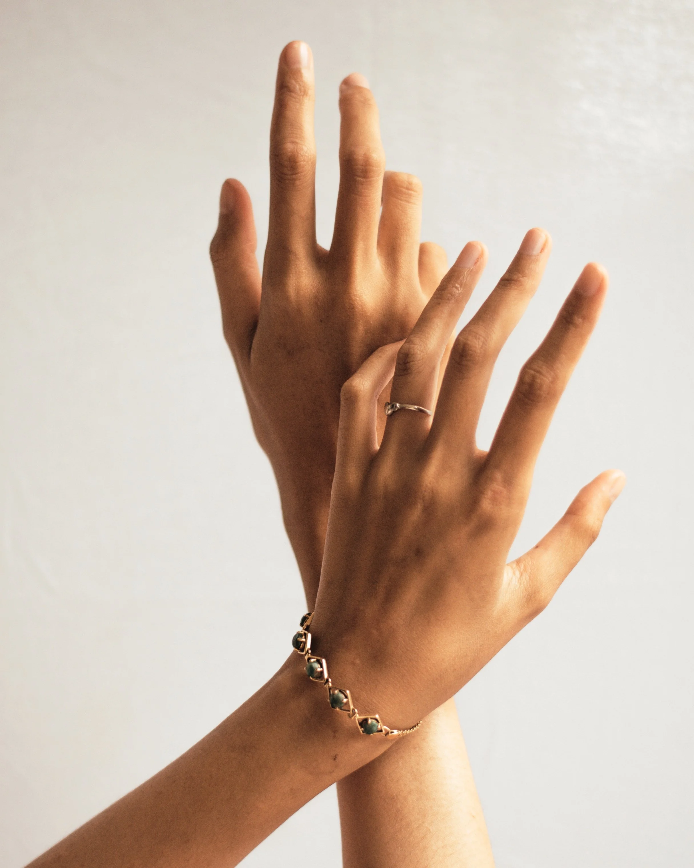 Deux mains féminines se touchent, l'une porte une bague et un bracelet.