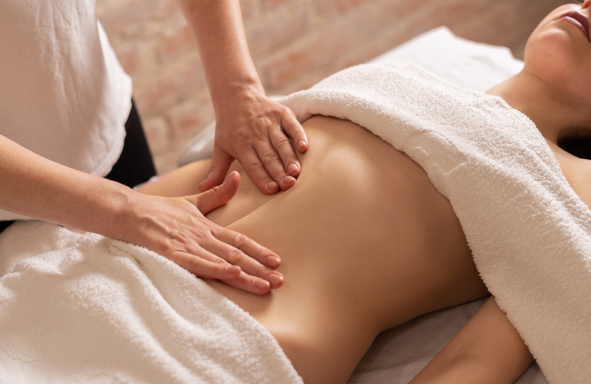 Personne recevant un massage relaxant dans un spa ou un centre de bien-être, partiellement couverte d'une serviette blanche.