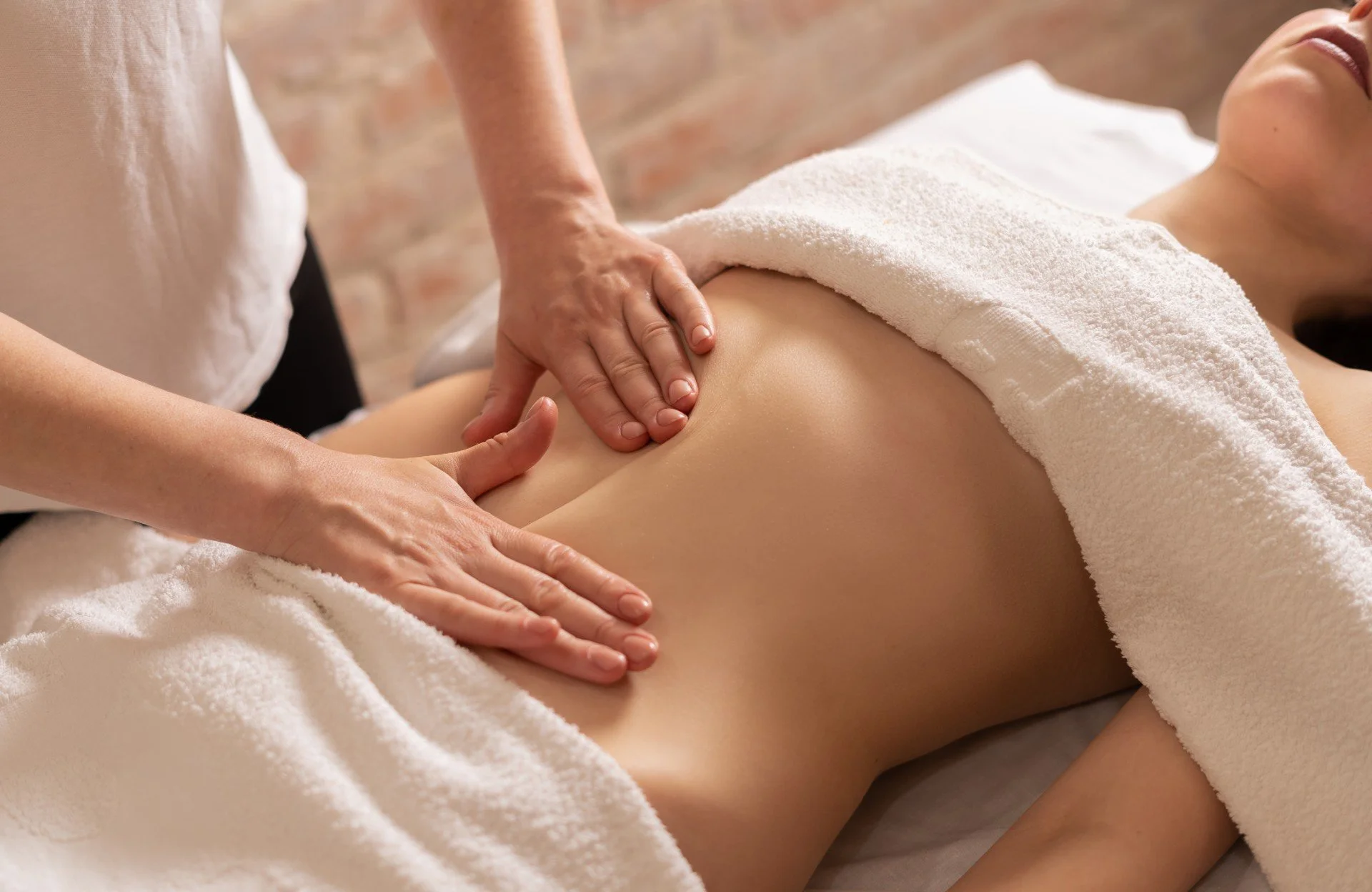 Une personne reçoit un massage à l'abdomen dans un spa, recouverte d'une serviette blanche.