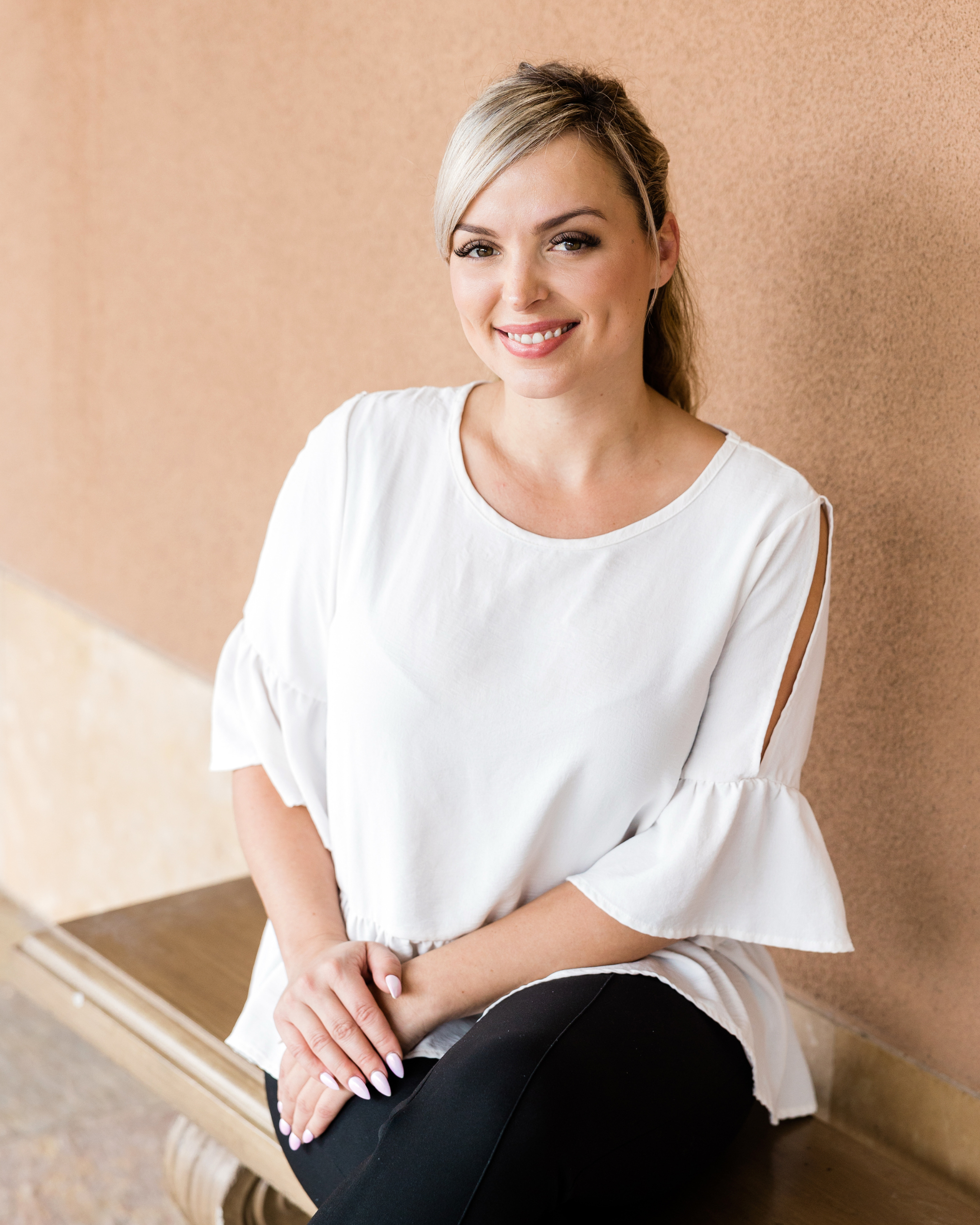 Une femme souriante assise sur un banc contre un mur beige.