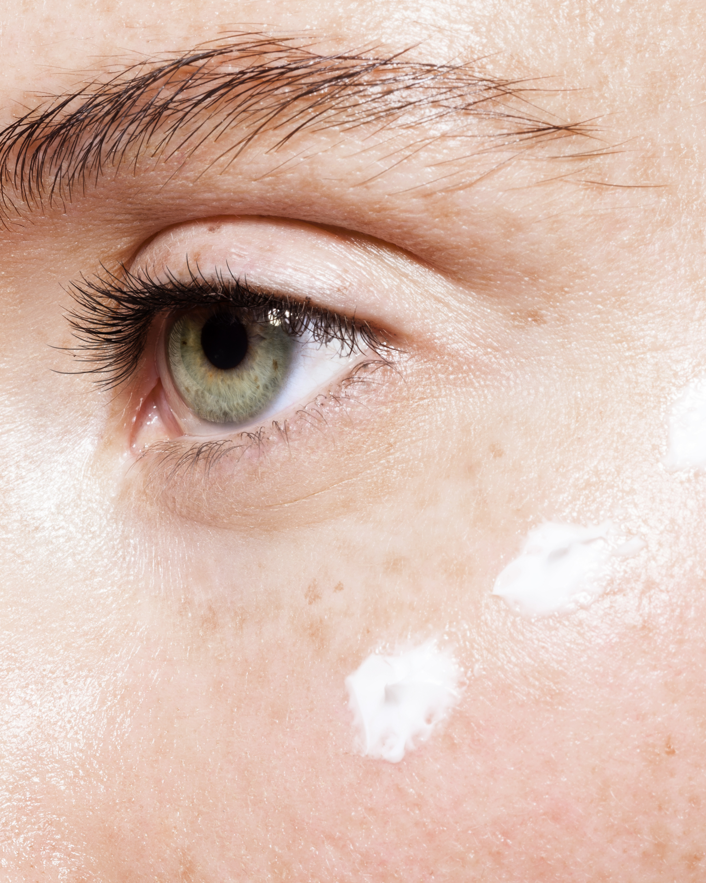Gros plan d'un œil vert humain avec des taches de crème ou de lotion sur la joue.