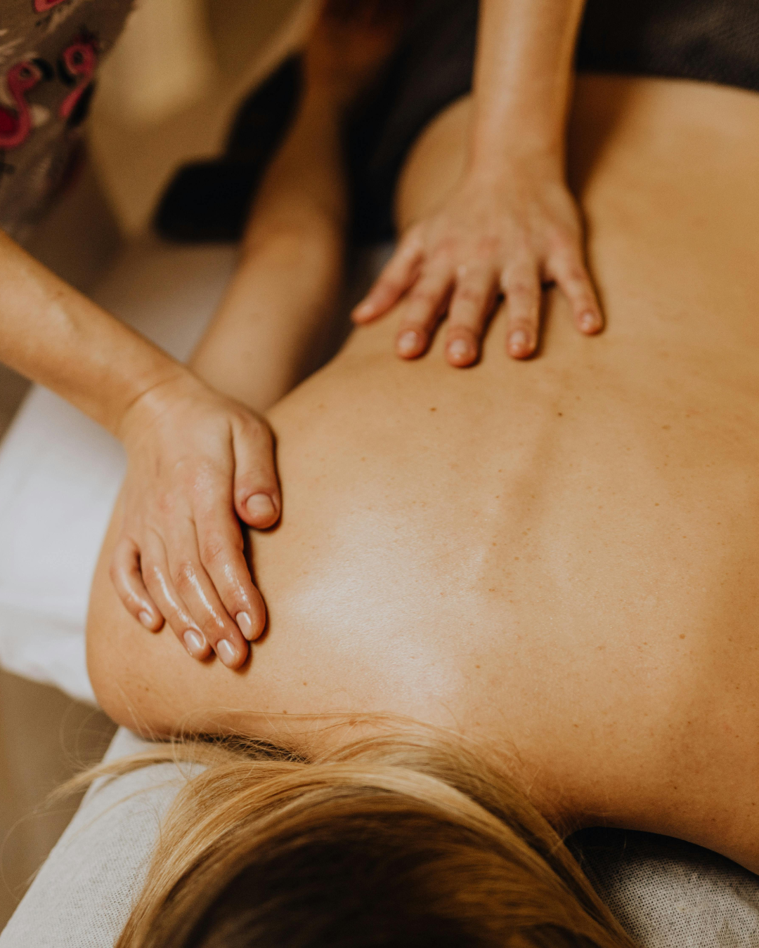 Une personne reçoit un massage du dos avec deux mains adultes, dans un cadre de spa ou de massage.