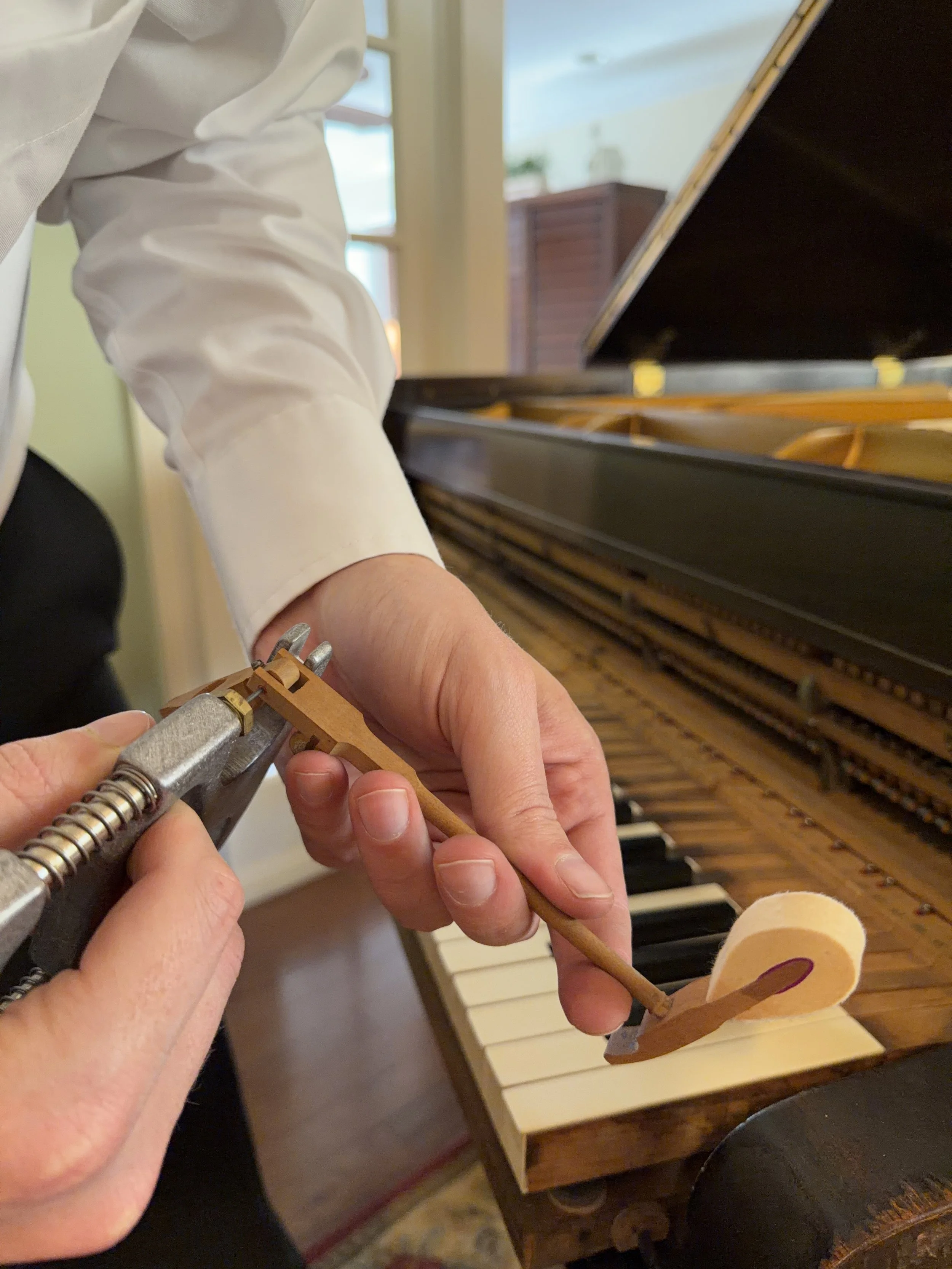Person adjusting a wooden balance with a metal clamp in front of an open piano.
