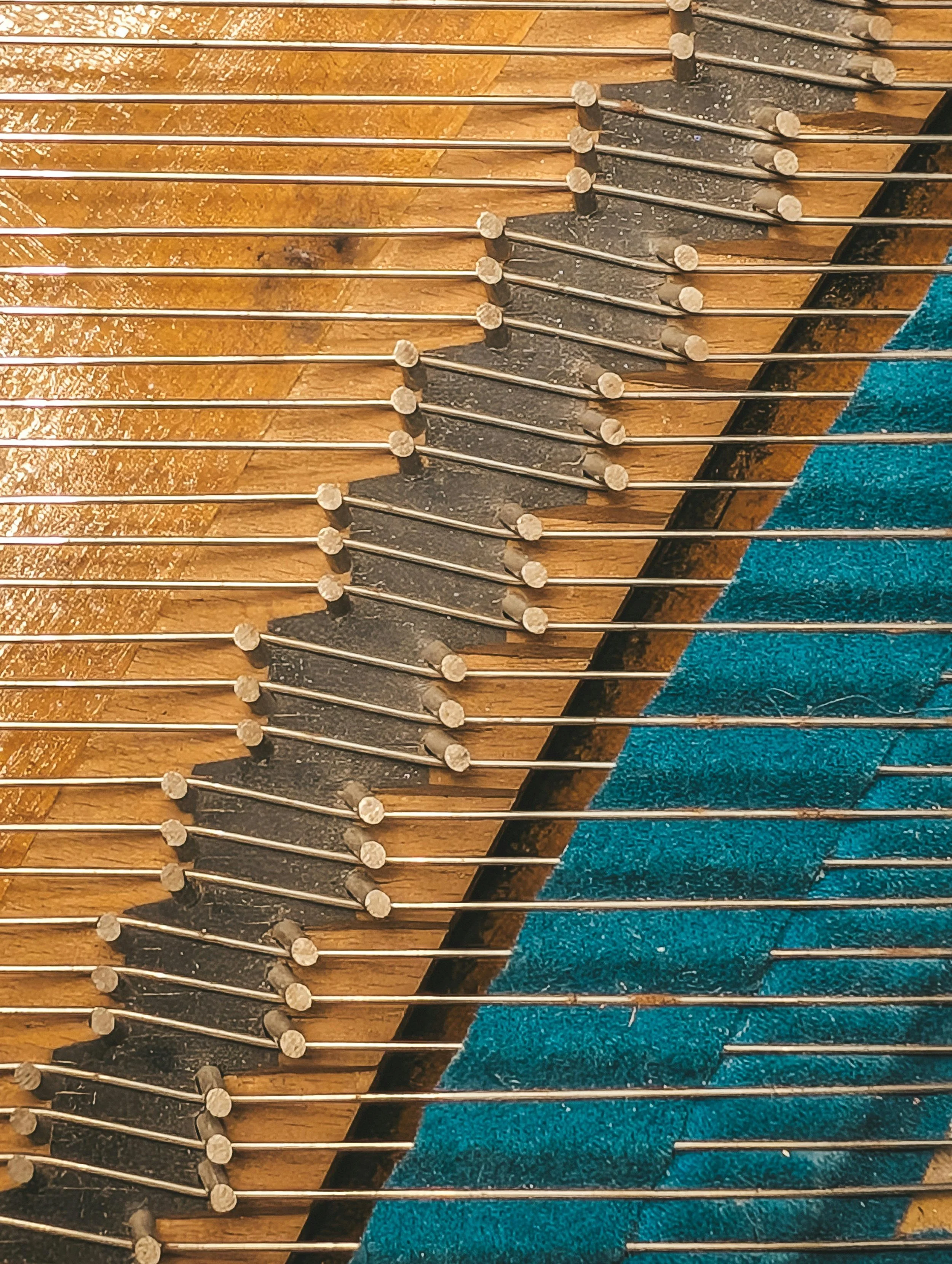 Close-up of the interior of a piano's soundboard with numerous tuning pins and strings, with a section of teal felt in the lower right corner.