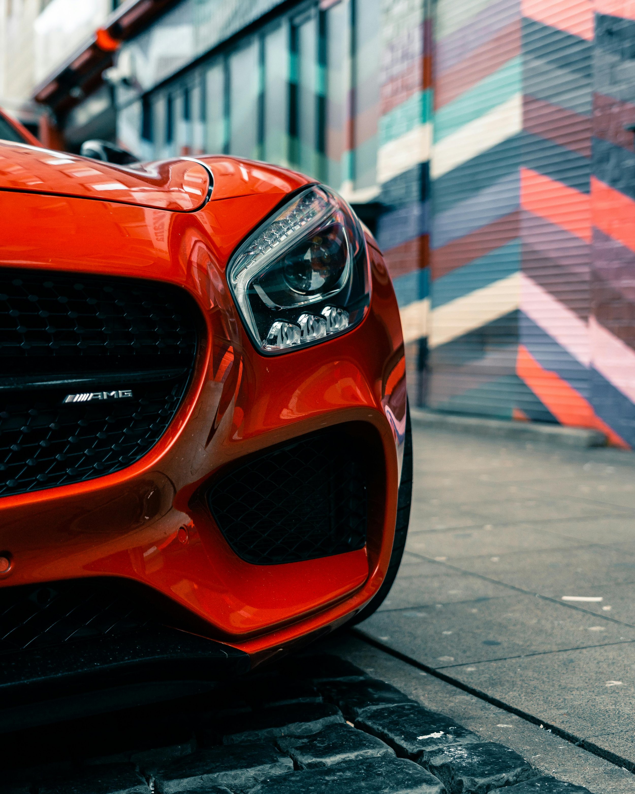 Close-up of a red luxury Mercedes-Benz AMG car parked on the street near a colorful mural.
