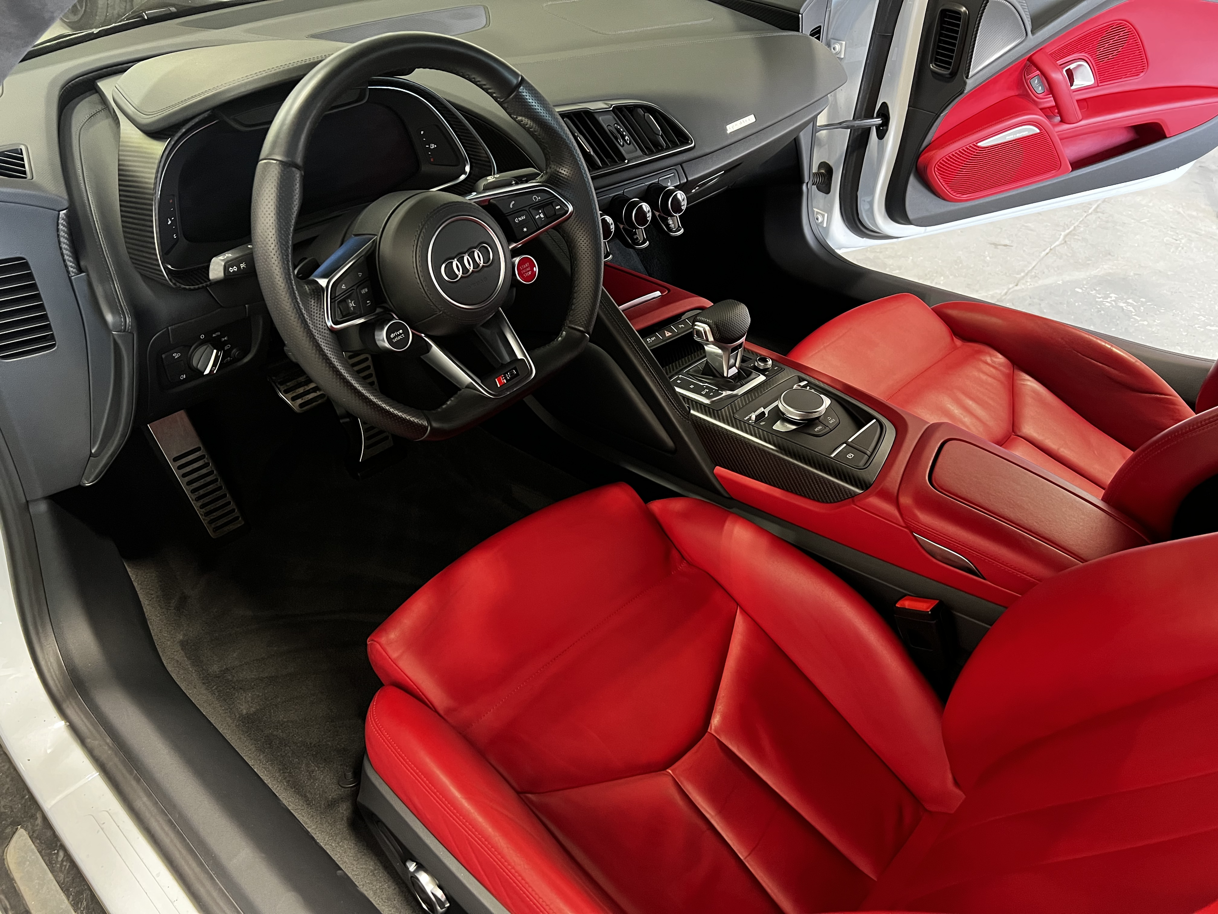 Inside the cockpit of a luxury Audi sports car with black and red interior, red leather seats, and a racing steering wheel.