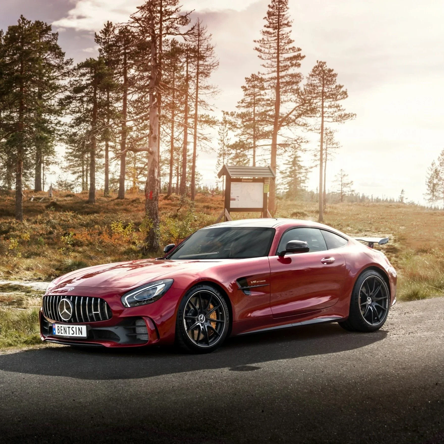 Red Mercedes-Benz sports car parked on side of the road with a forest background and a signpost.
