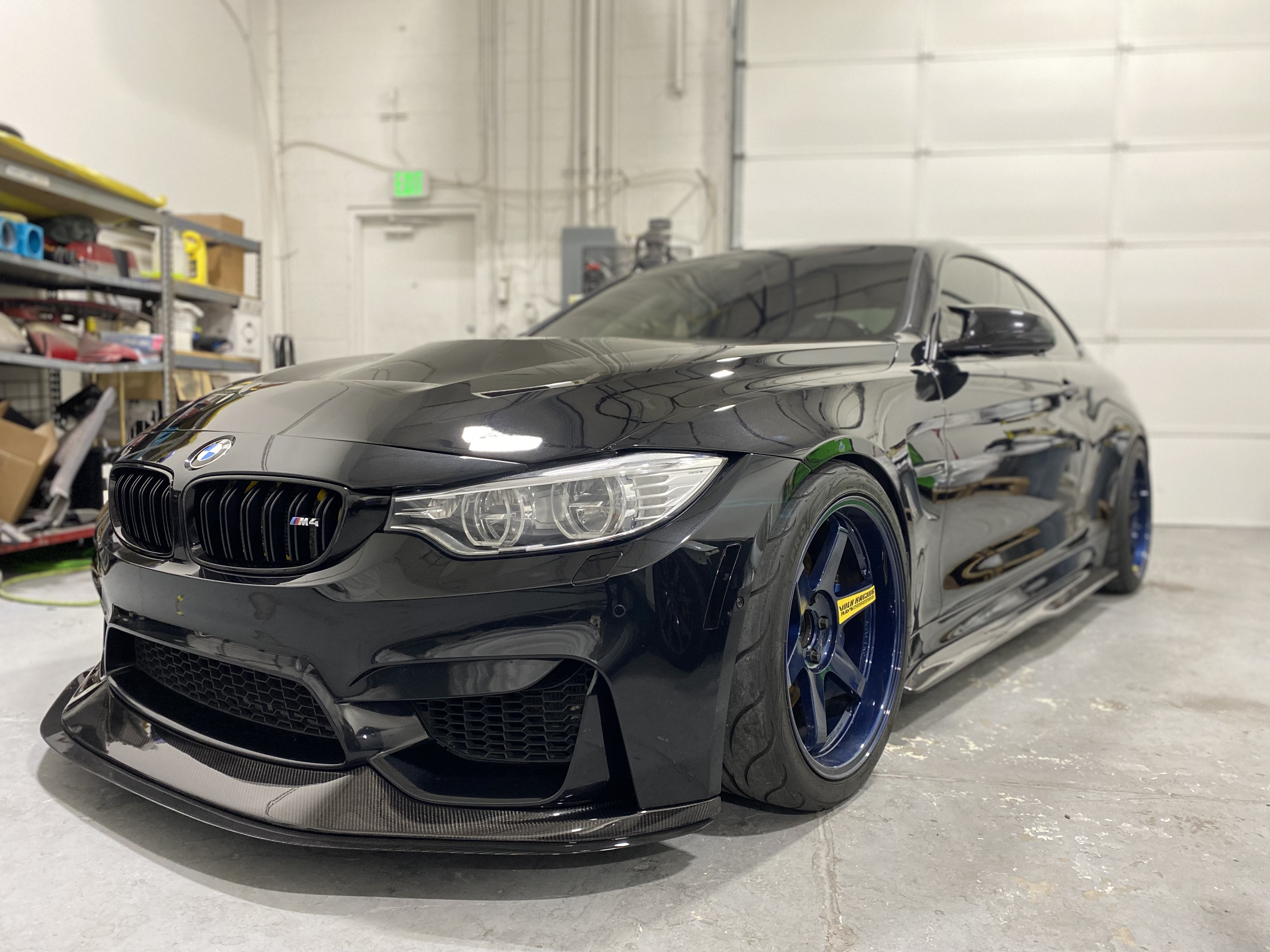 Black BMW M4 sports car with blue wheels inside a garage.