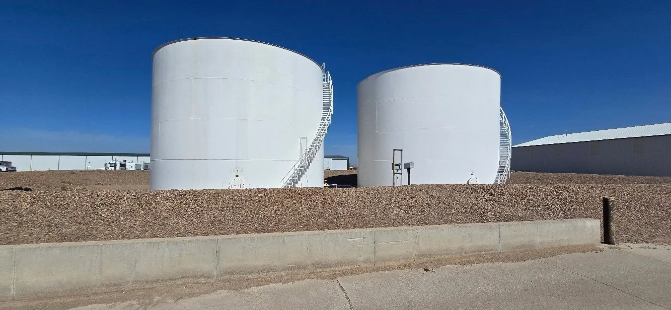 Two large white storage tanks with exterior staircases on a gravel lot