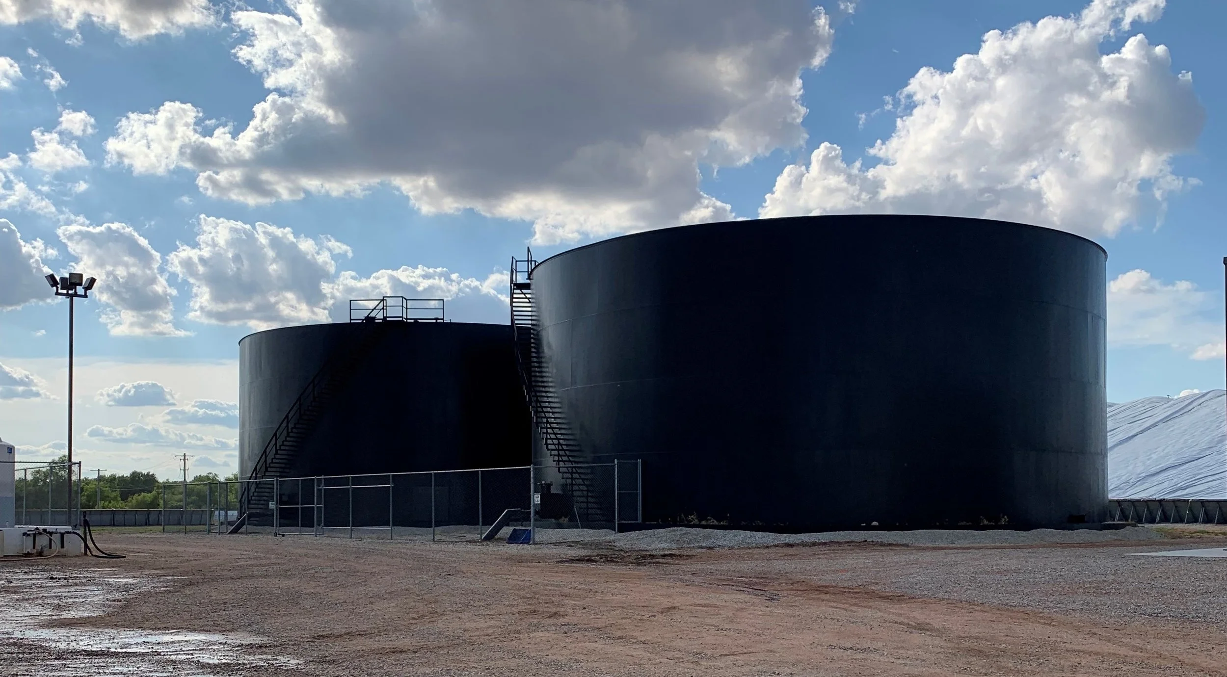 Two large black industrial tanks with stairs and railing outside, under a partly cloudy sky.