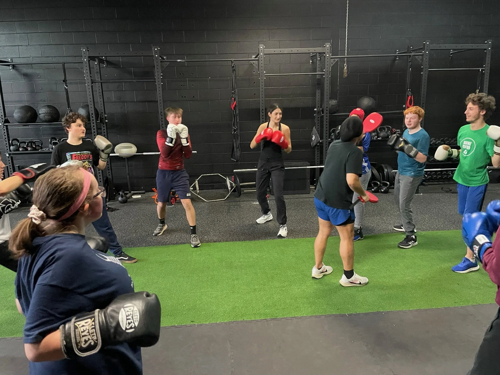 People participating in a boxing class or training session in a gym, wearing gloves and boxing gear.
