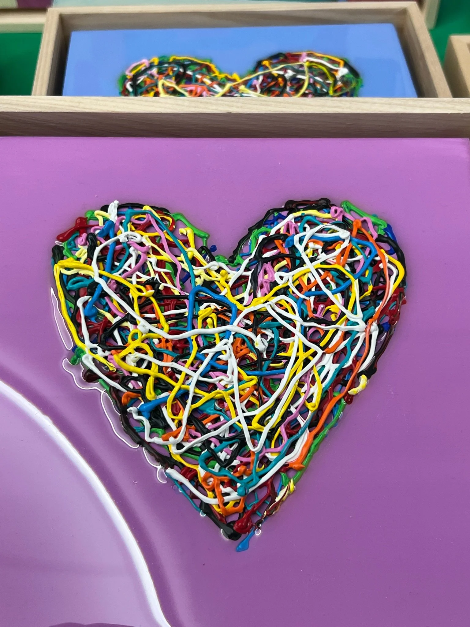 Colorful heart-shaped artwork made of tangled rubber bands on a purple background.