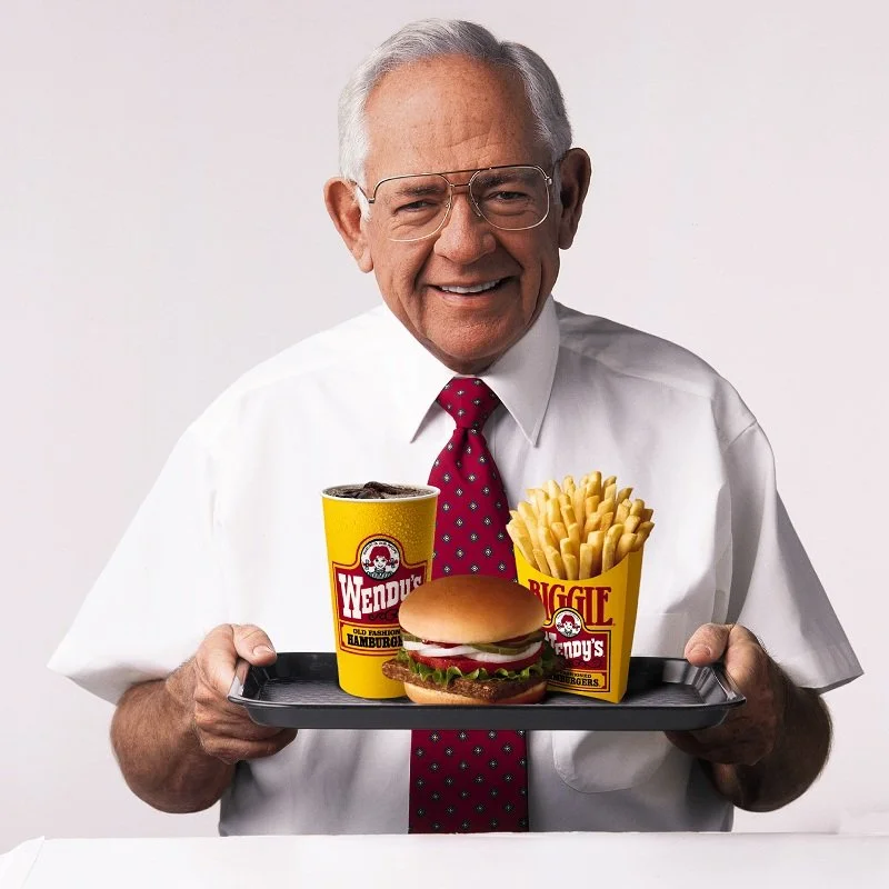 Dave Thomas holding a tray with Wendy's food, including a hamburger, French fries, and a soda