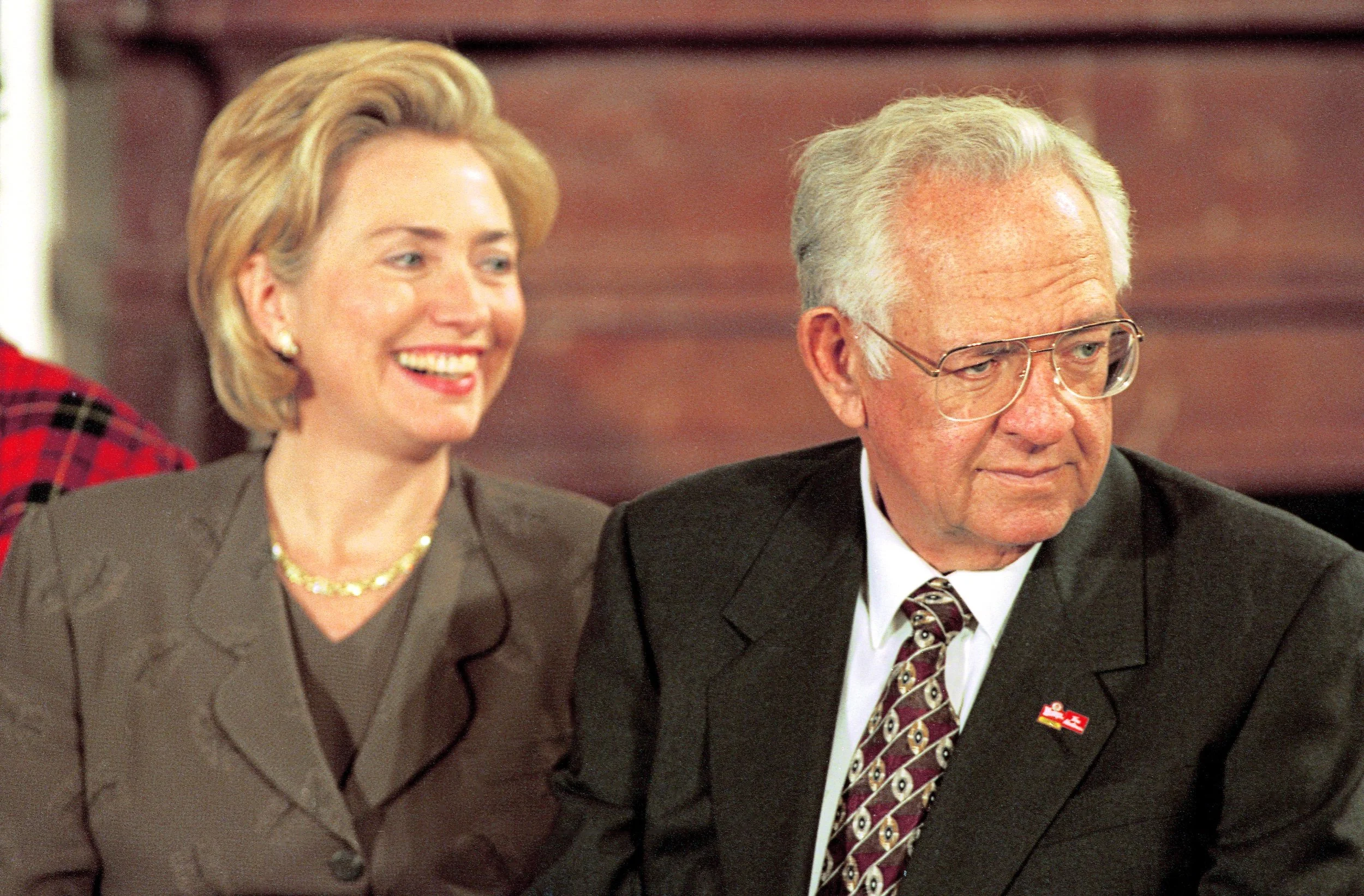 A woman and an elderly man sitting next to each other in formal clothing, smiling and appearing to be at a formal event or gathering.