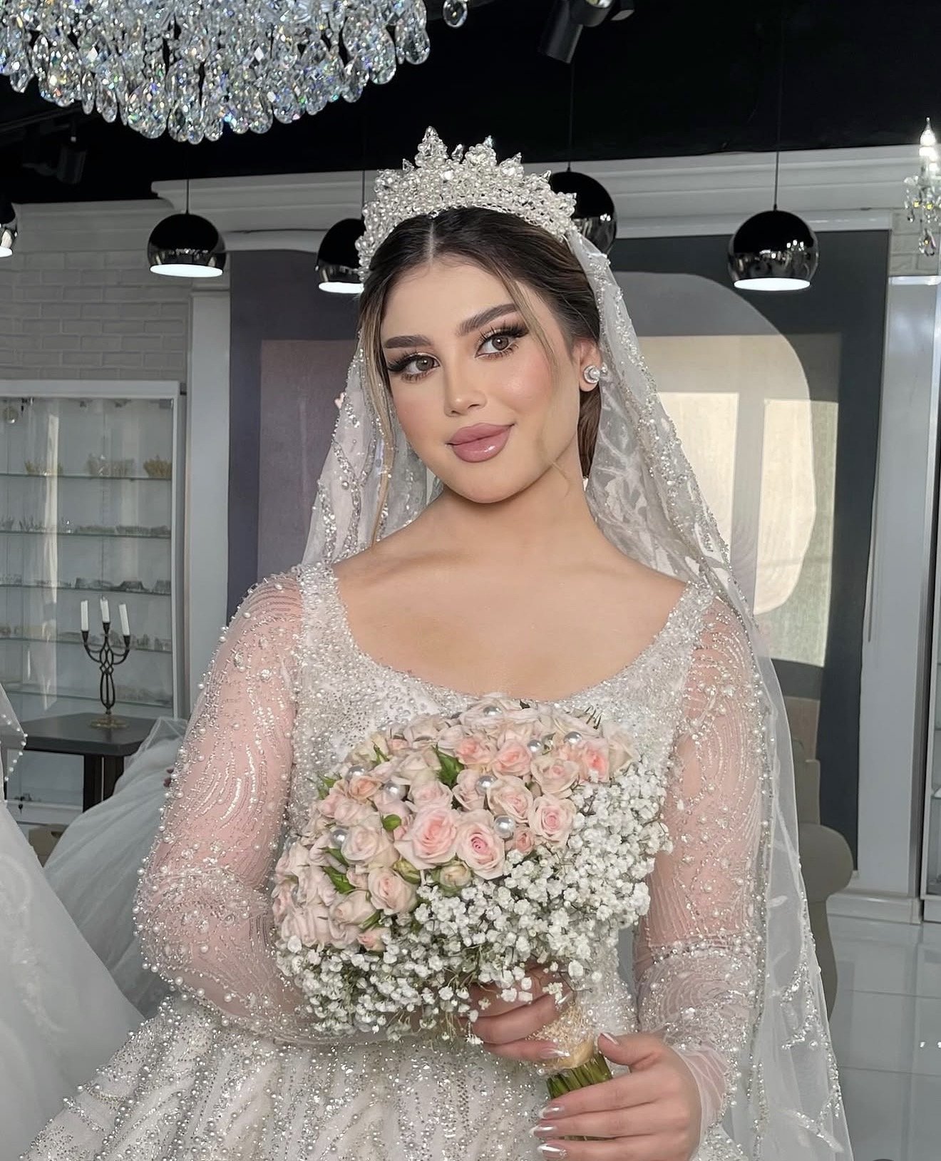 A bride in a white wedding gown holding a bouquet of pink roses and white baby's breath.