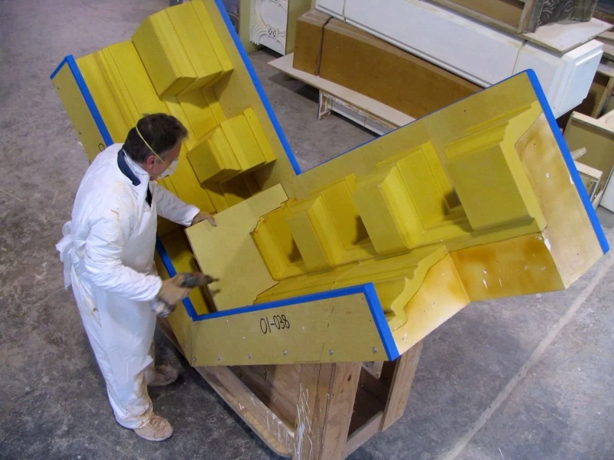 A production laminator in a white suit and gloves is modifying a mold of dentils on a pediment. PGRG