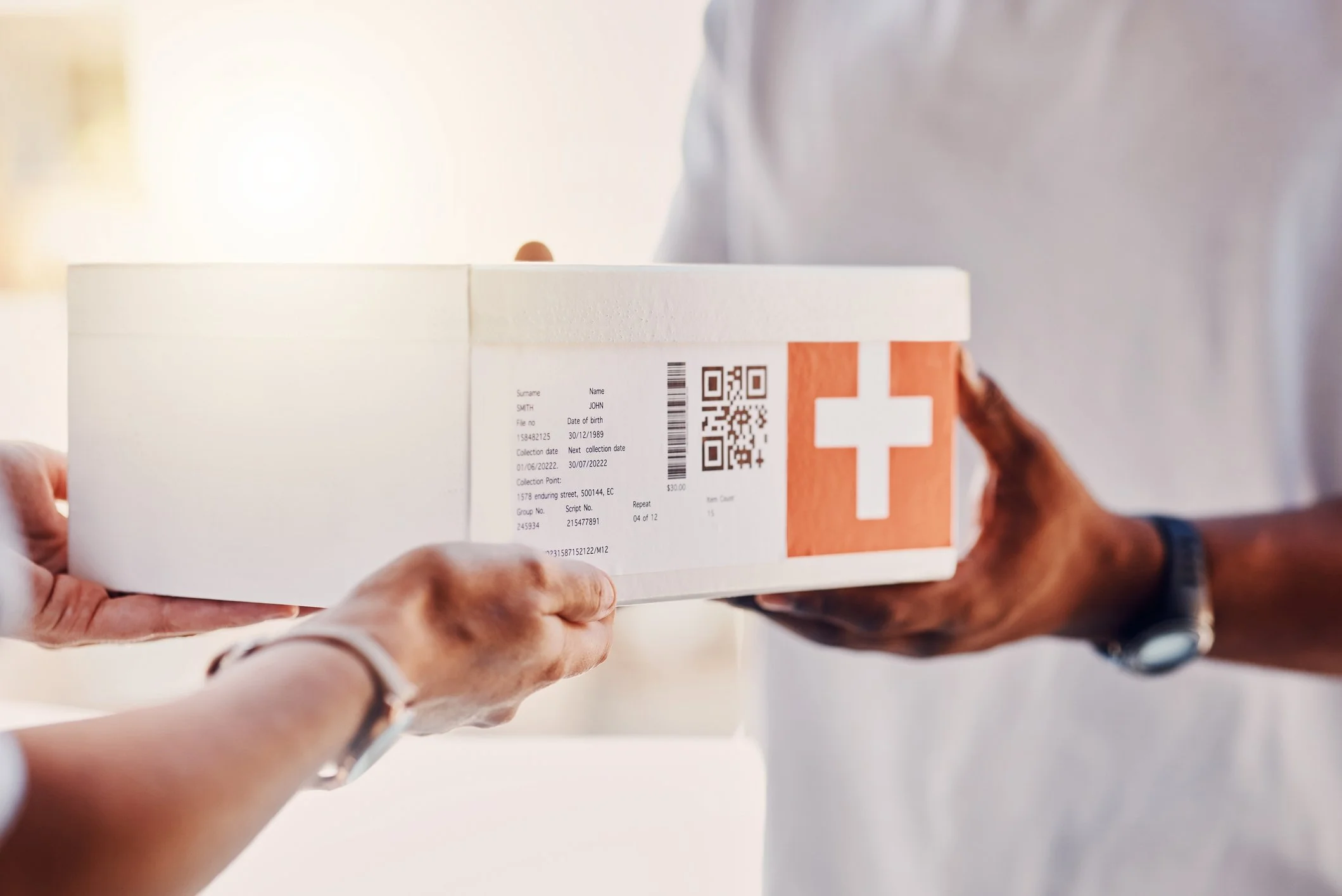 Two people exchanging a white box with a Swiss flag symbol and a label, one person handing it over and the other receiving it, both wearing wristwatches.