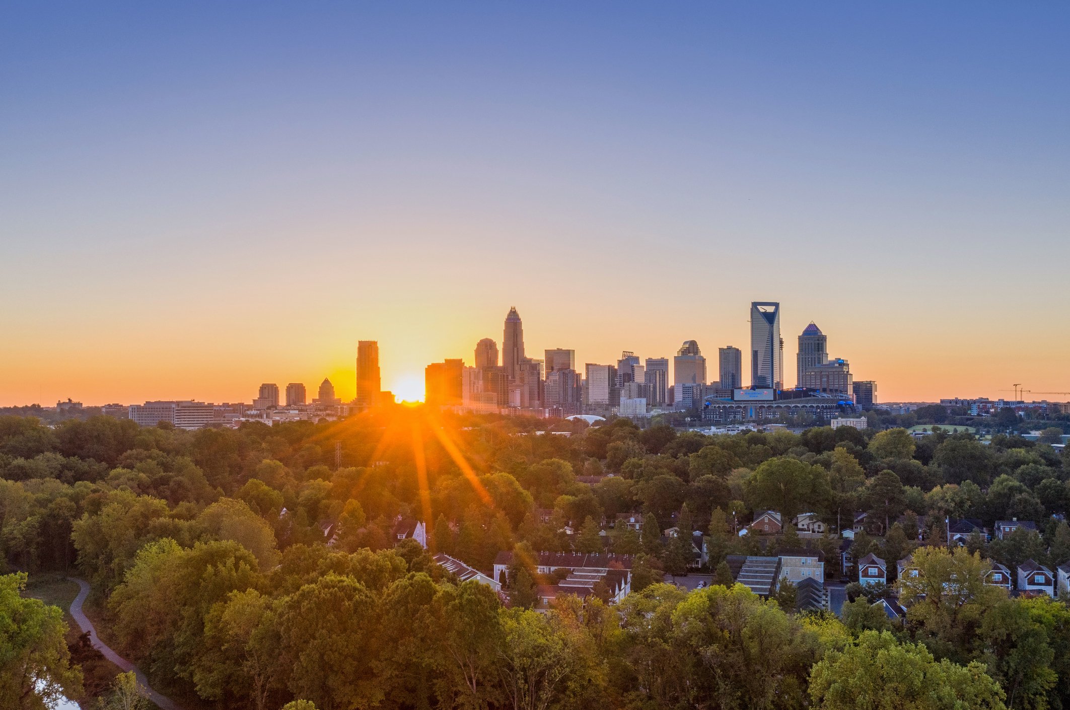 Sunset over the skyline of Charlotte, North Carolina, with trees in the foreground and a clear sky.