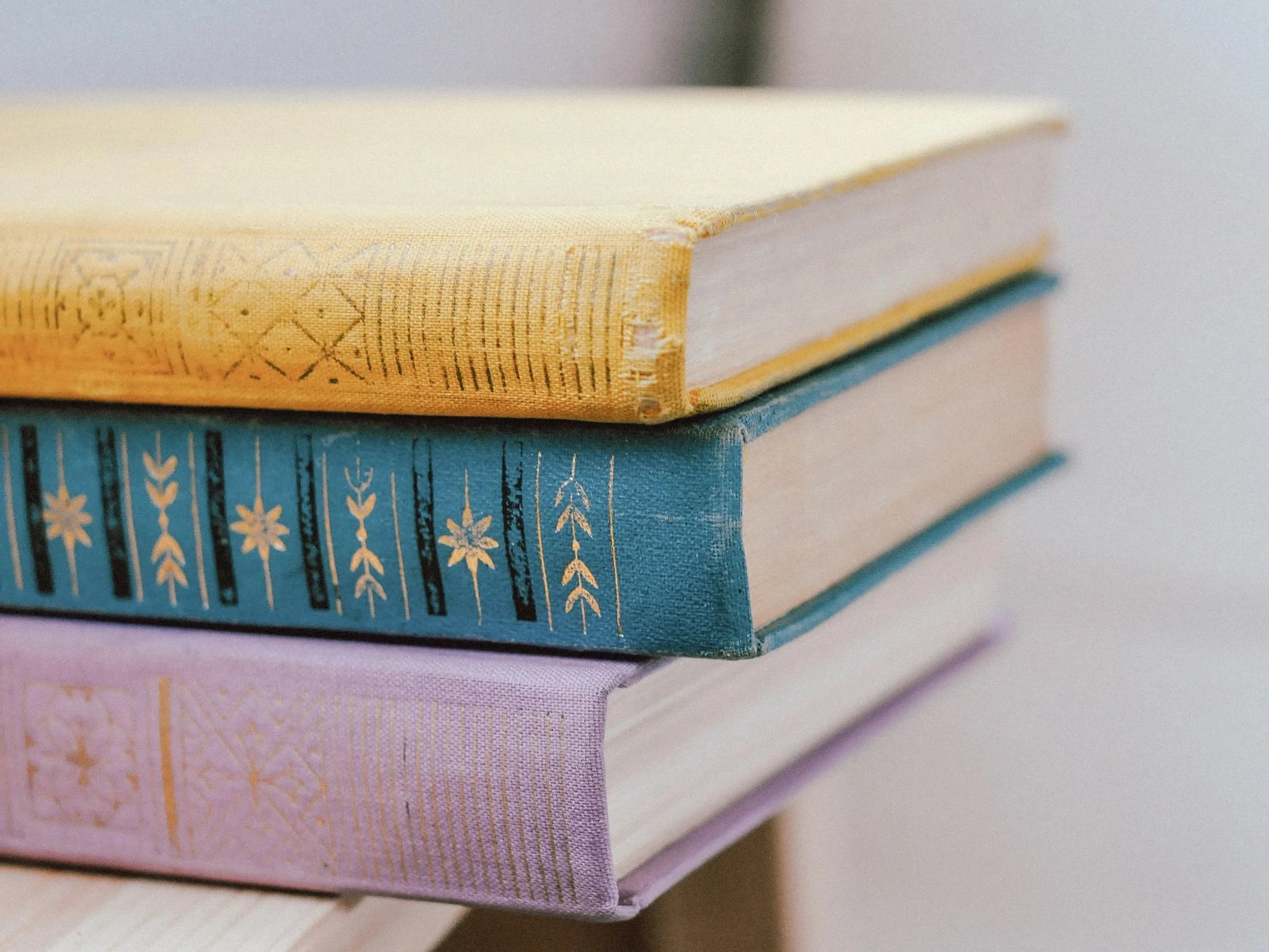 Stacked hardcover books with decorative spines in pastel colors including yellow, blue, and pink.