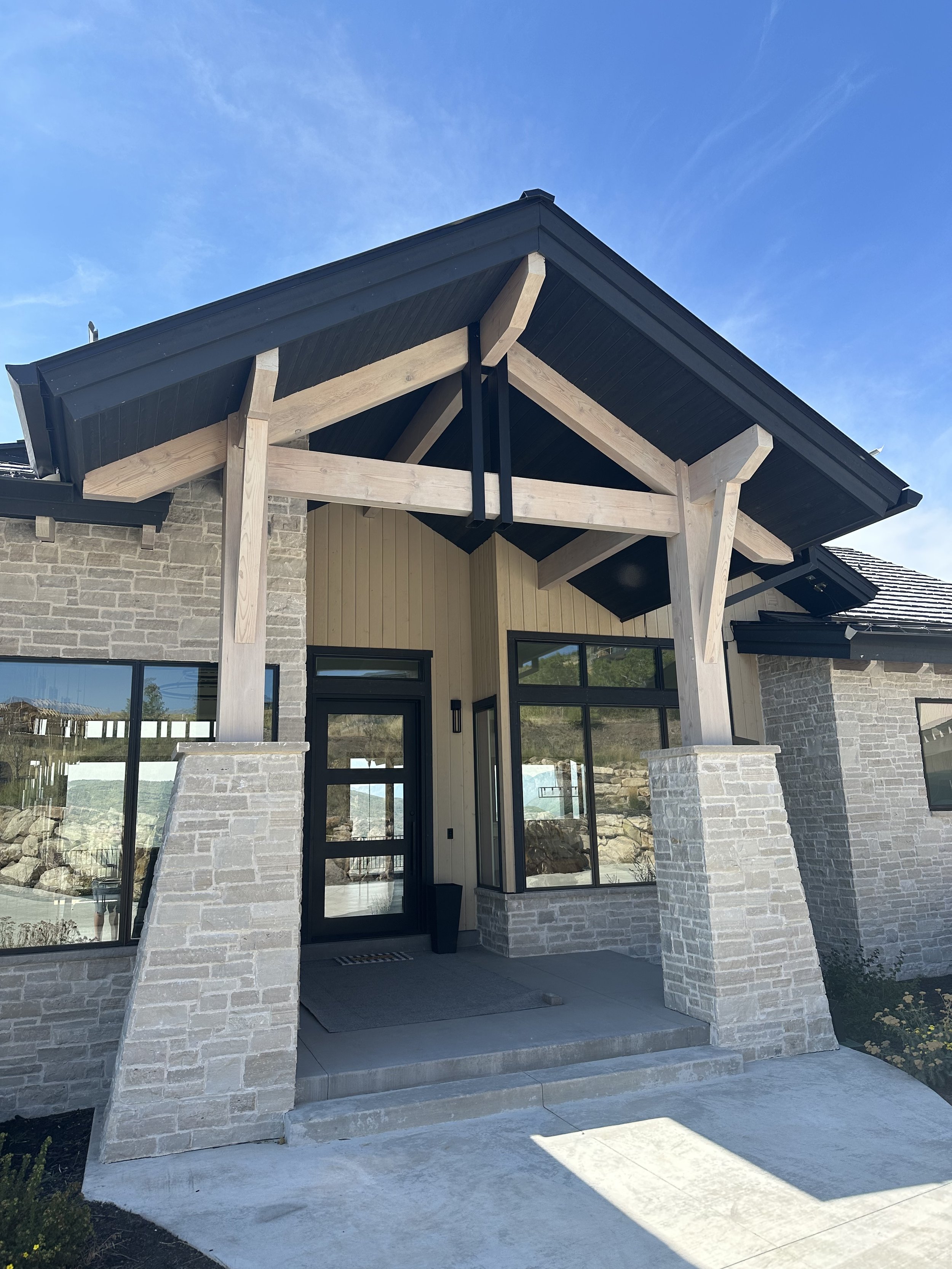 Front view of a modern house with timber beams on the exterior, and a covered porch pergola with heavy timber supports. 