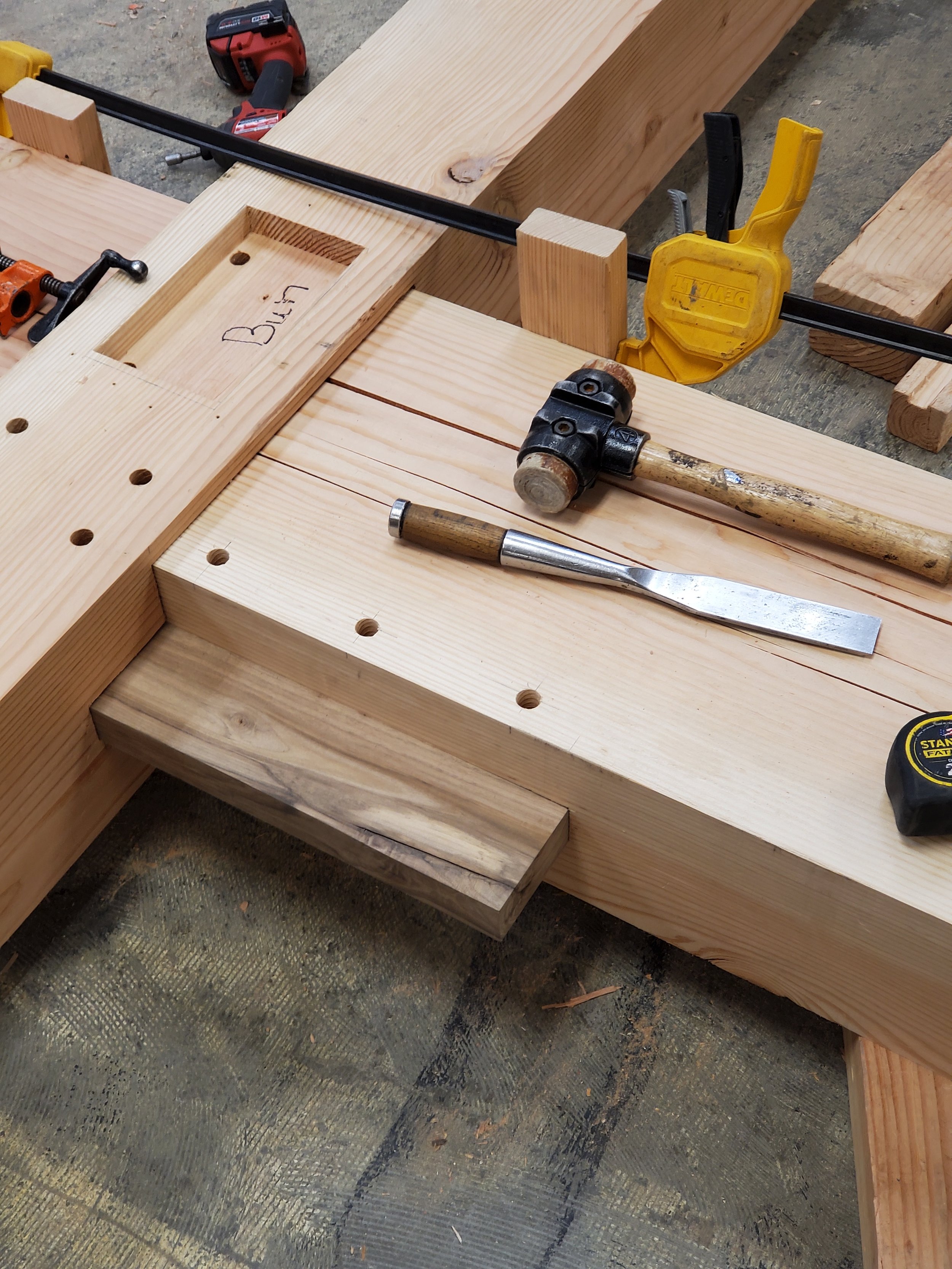 Woodworking workspace with a hammer, chisel, clamps, and pieces of timber, with the word 'Build' written inside a cutout in the wood.