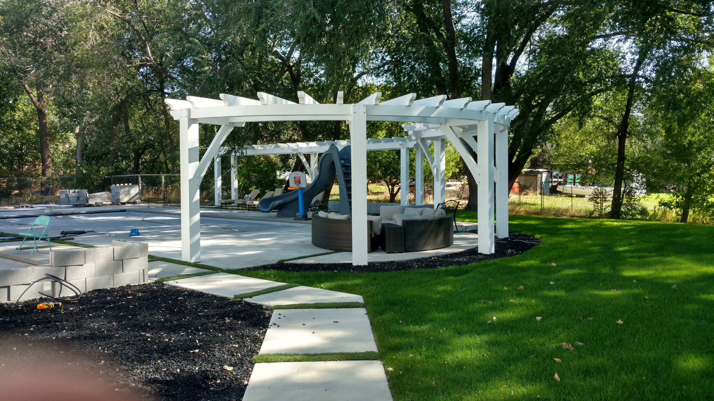 Modern white backyard pergola install shading the pool and patio. 