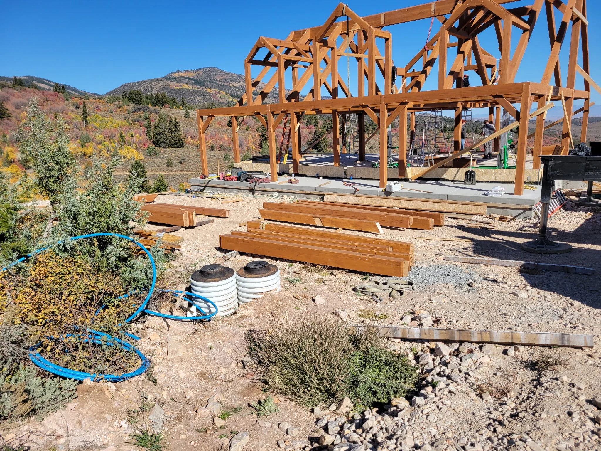 Construction site with wooden framing for a building set against a mountainous landscape with fall colors.