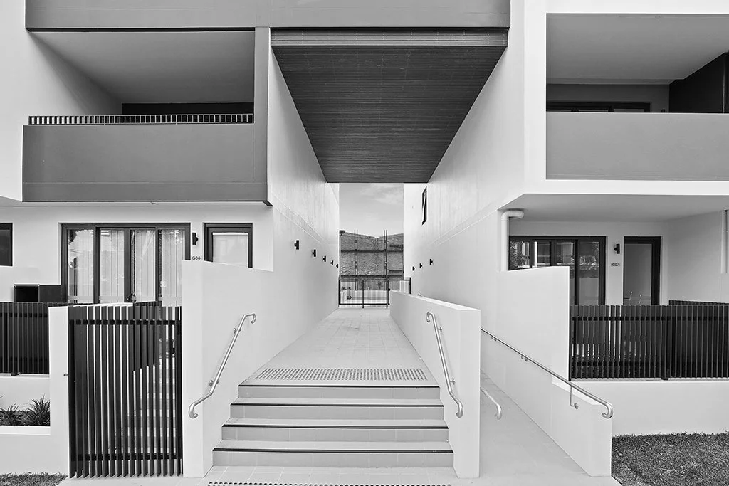 Modern white apartment complex with stairs and ramps, balconies, and glass doors.