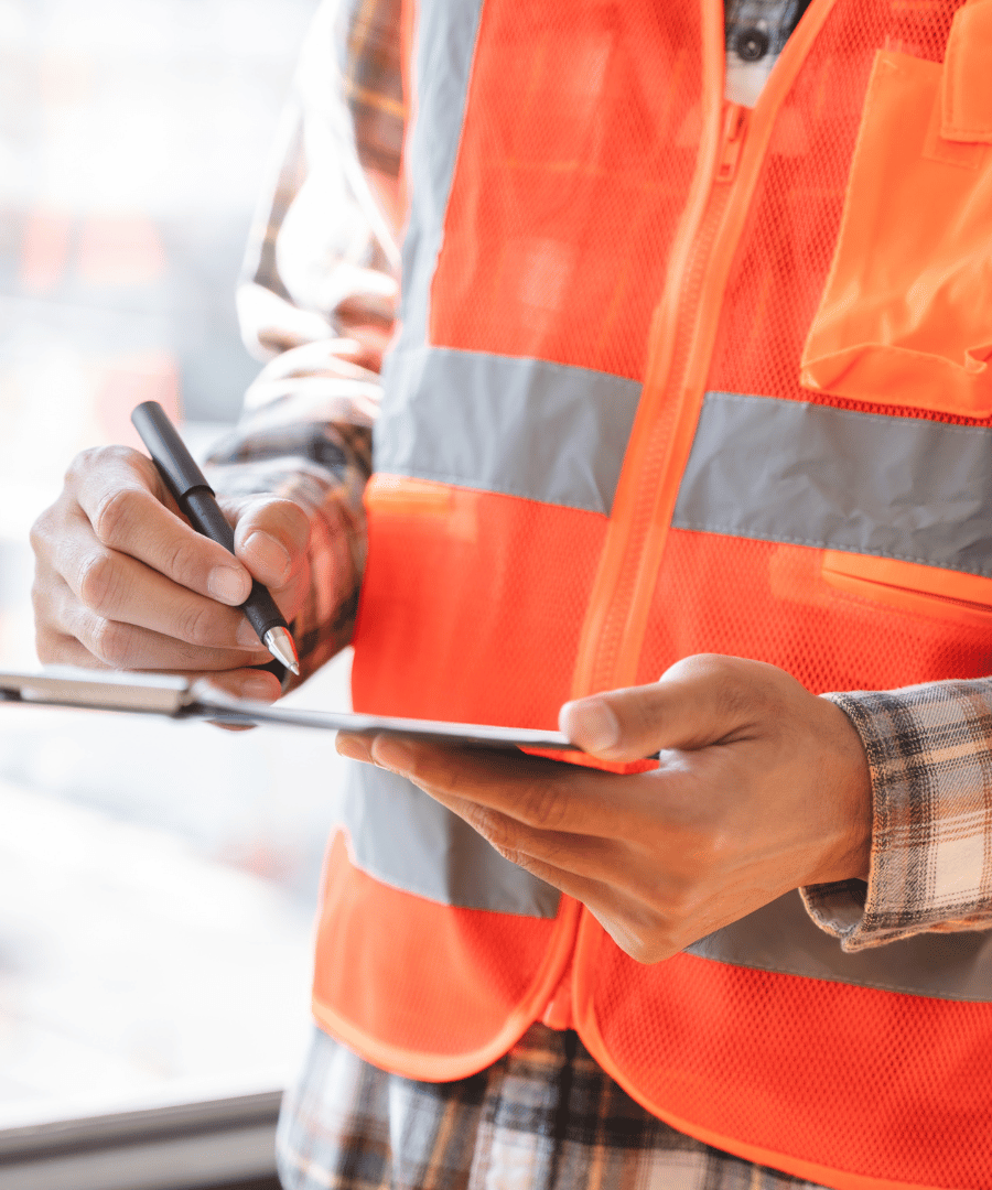 Person in orange safety vest holding a clipboard and writing with a pen.