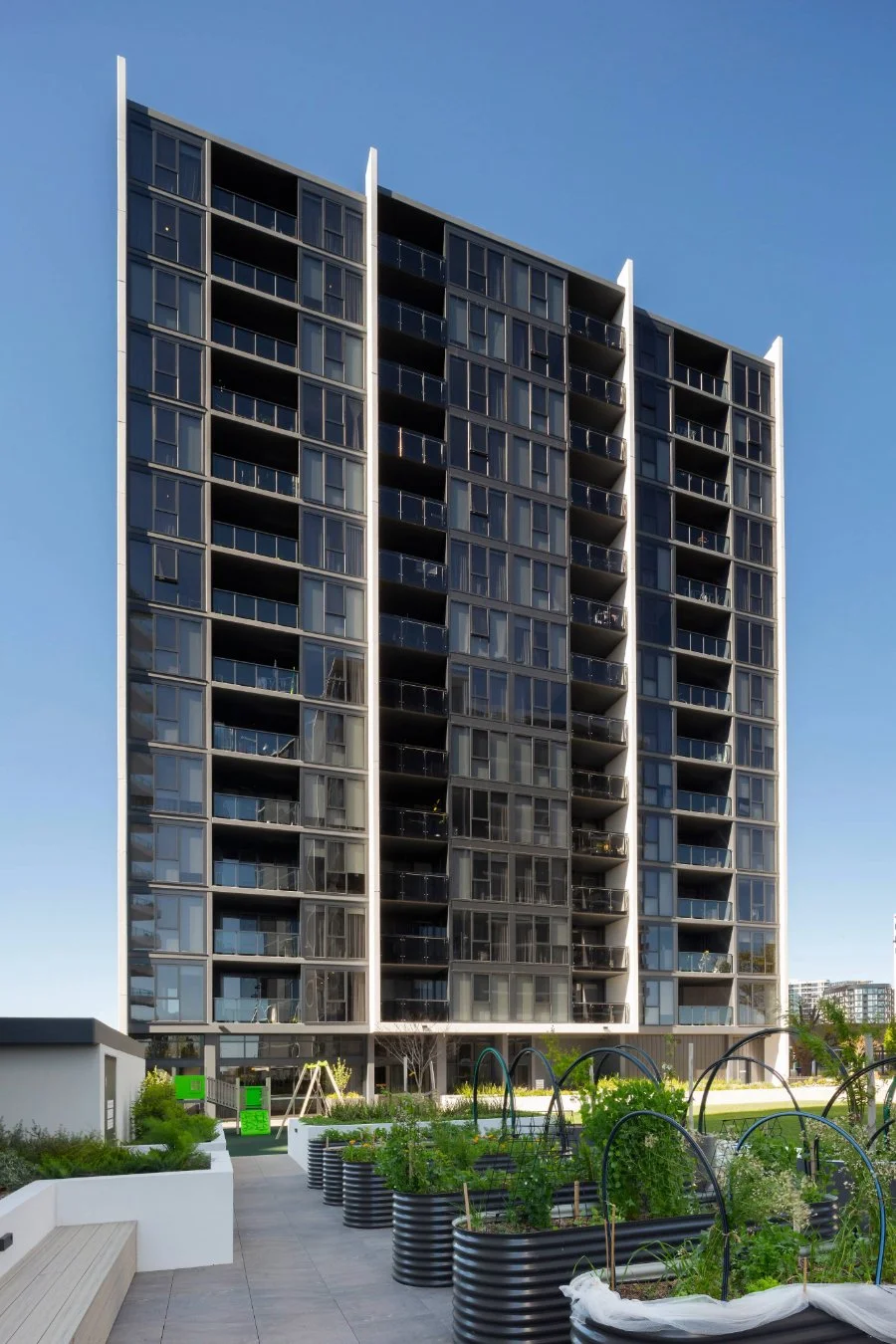 Modern multi-story apartment building with glass balconies and a landscaped courtyard in foreground.