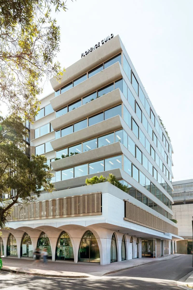 Modern multi-story building with large glass windows, horizontal balconies, and an arched storefront at the ground level.