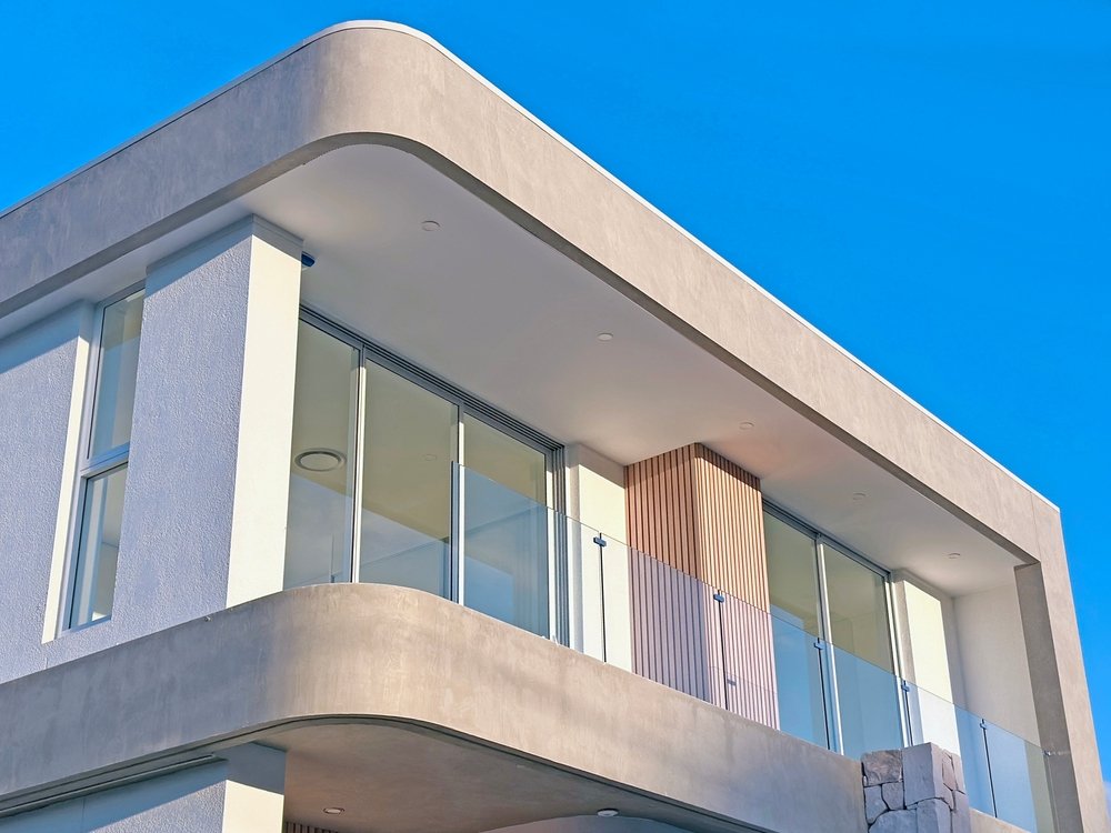 Modern building with large glass windows and a rounded corner, set against a clear blue sky.