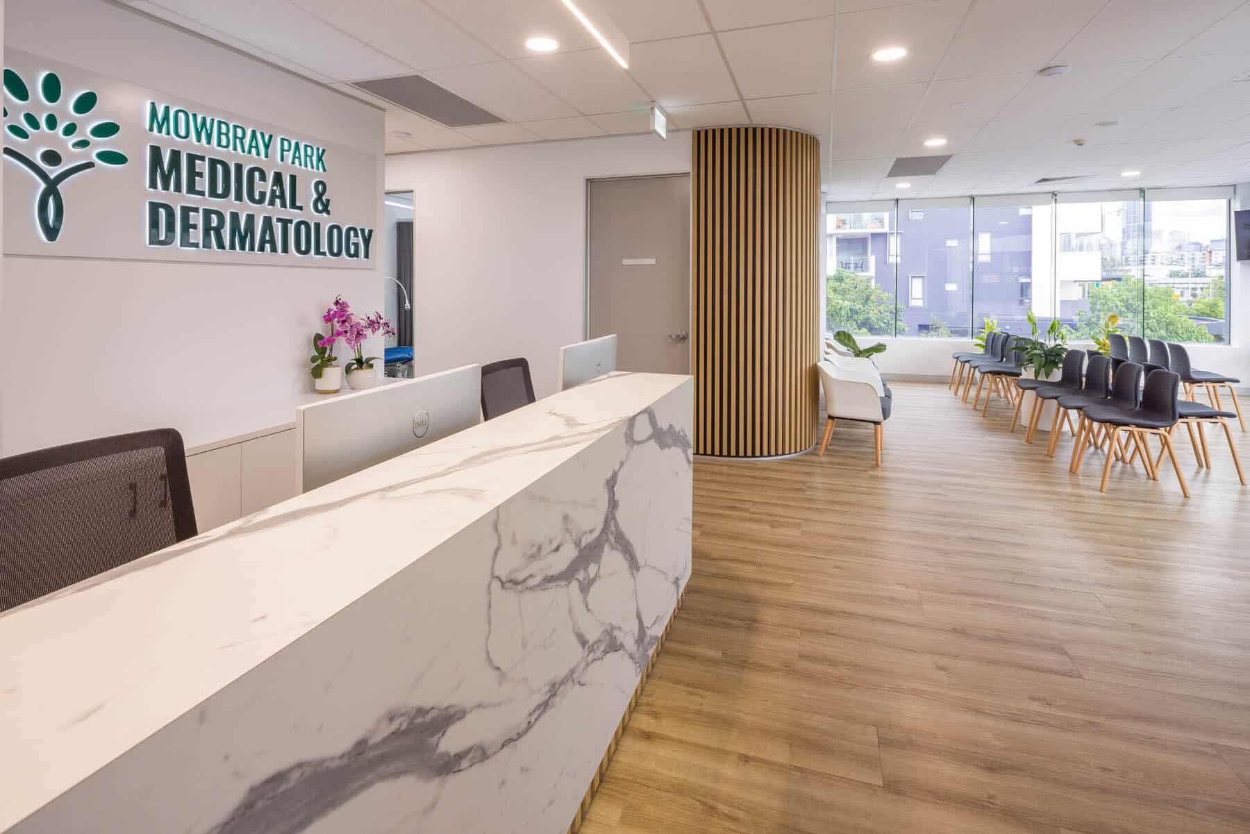 Reception area at Mowbray Park Medical & Dermatology with a marble counter, potted orchids, a waiting area with chairs and plants near large windows.