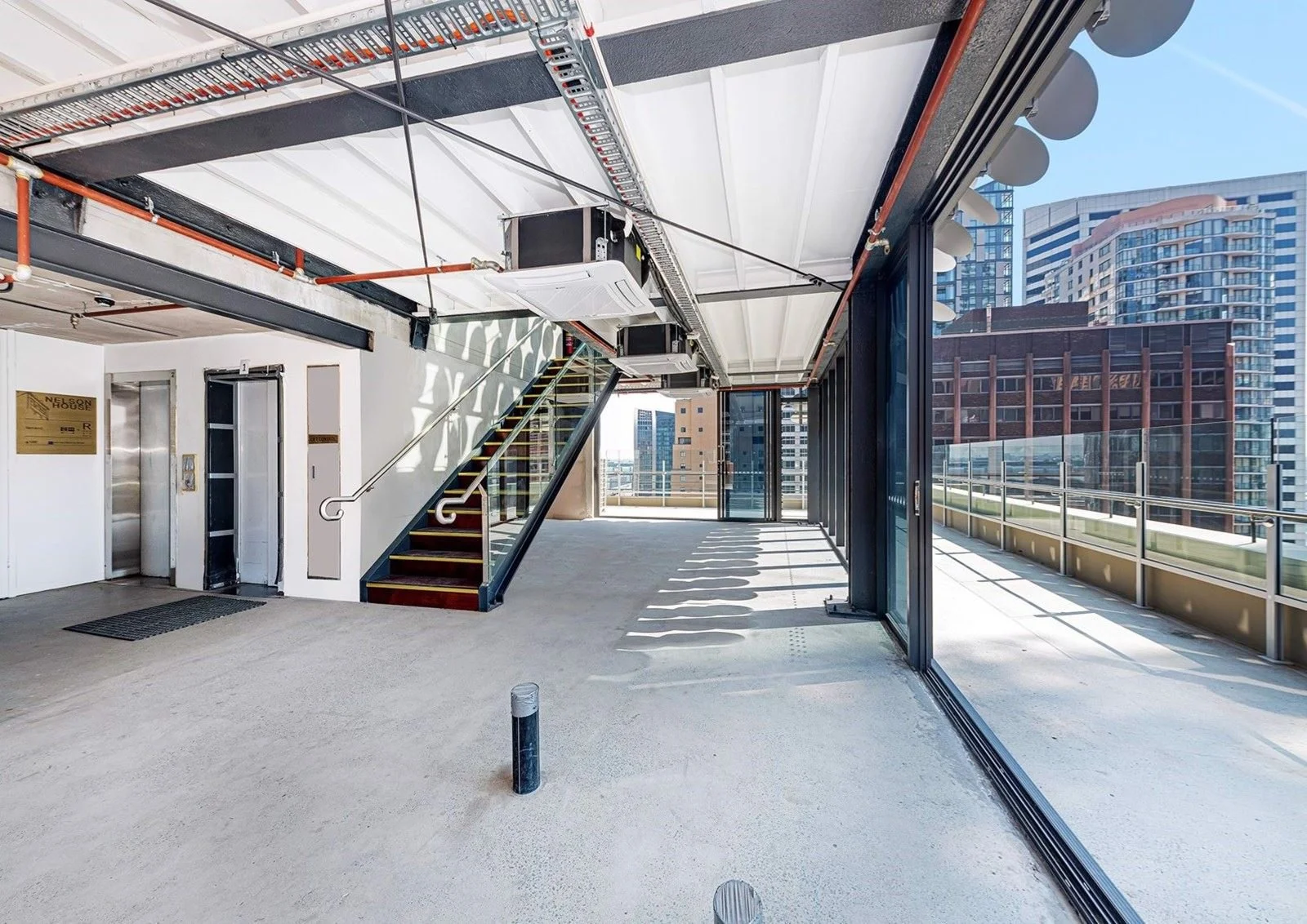 Empty outdoor balcony or terrace area with glass doors, stairs, and cityscape view of tall buildings.