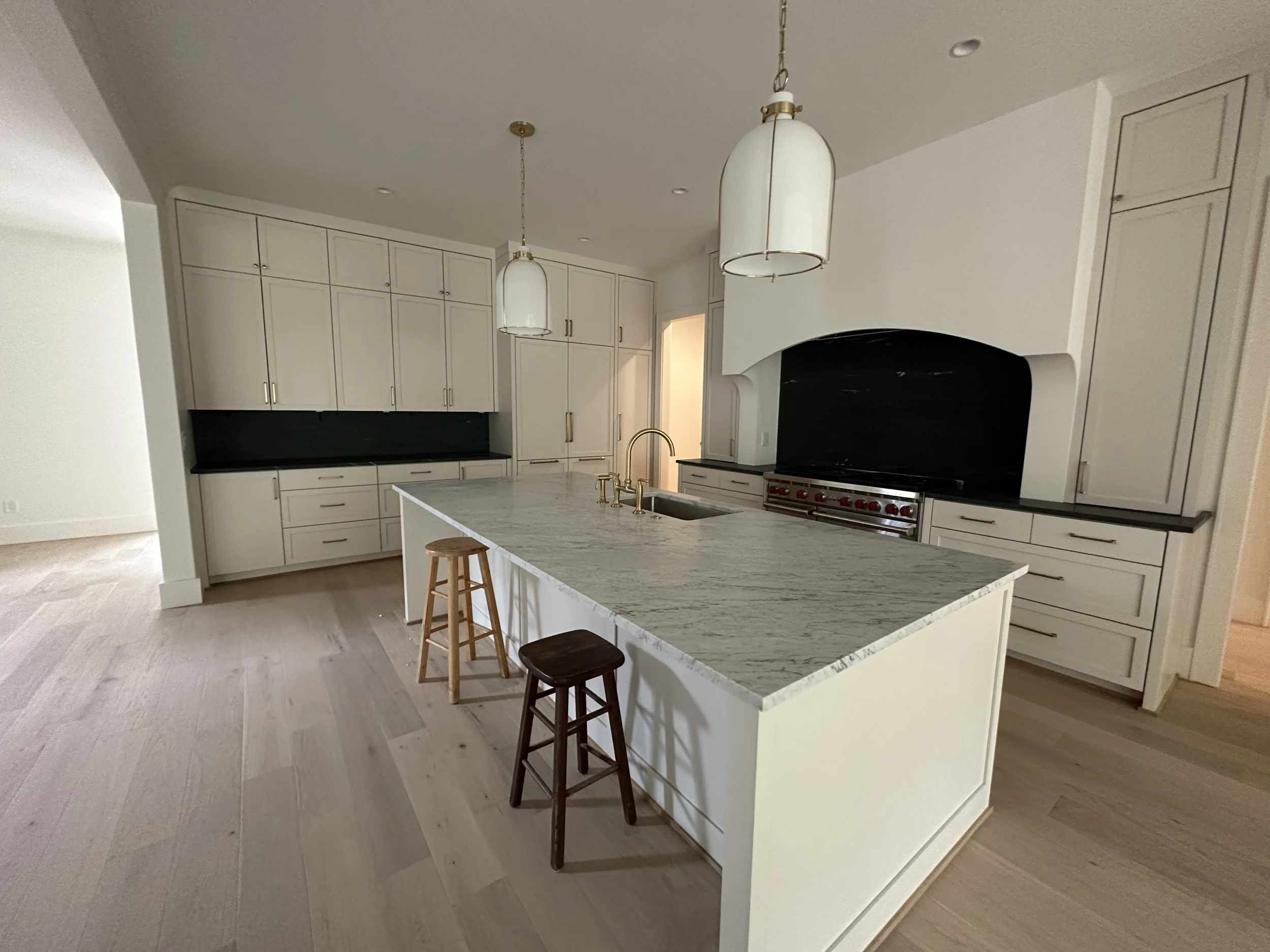 Modern kitchen with white cabinets, a marble island, pendant lights, and a black stovetop with oven surrounded by cabinetry.